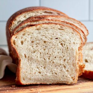 A loaf of sourdough potato bread cut into slices on a cutting board.