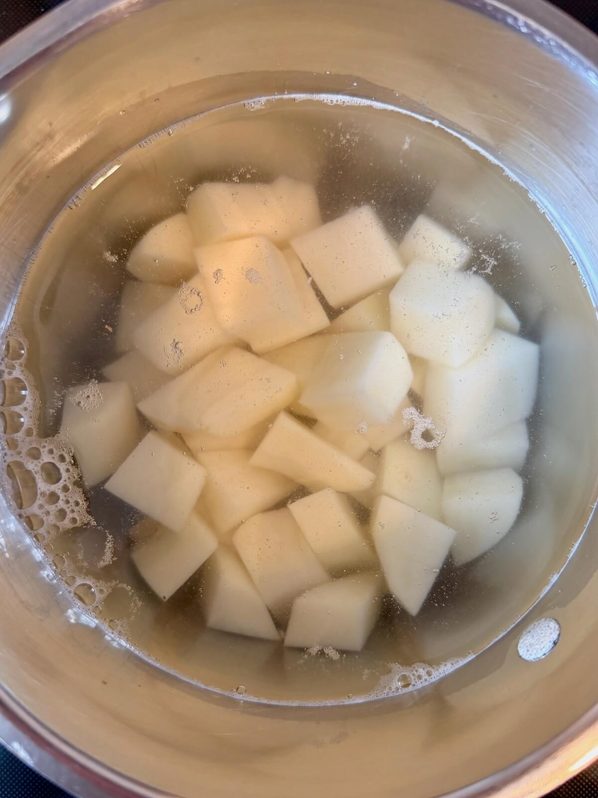 Peeled and cubed potatoes submerged in water in a stainless steel pot.