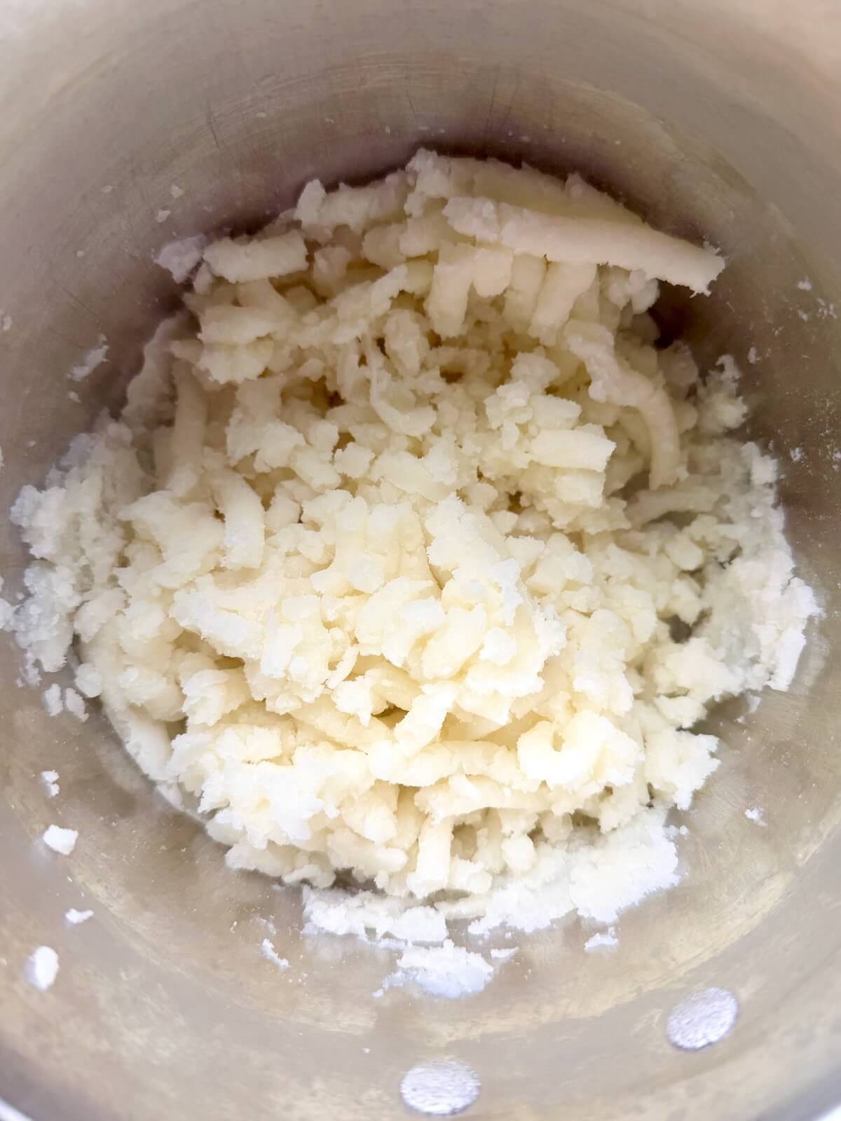 Boiled potatoes mashed in a stainless steel pot.