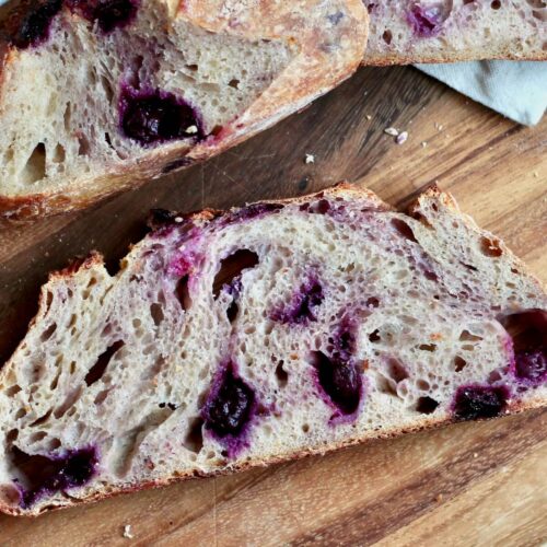 Slices of lemon blueberry sourdough bread on a wooden cutting board.
