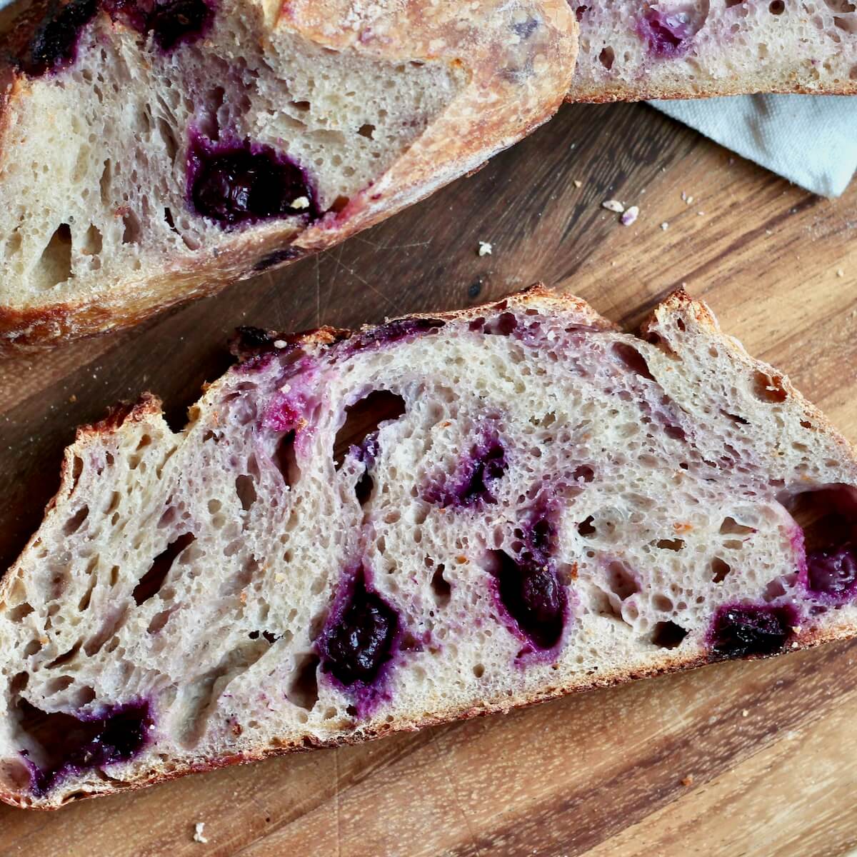 Slices of lemon blueberry sourdough bread on a wooden cutting board.