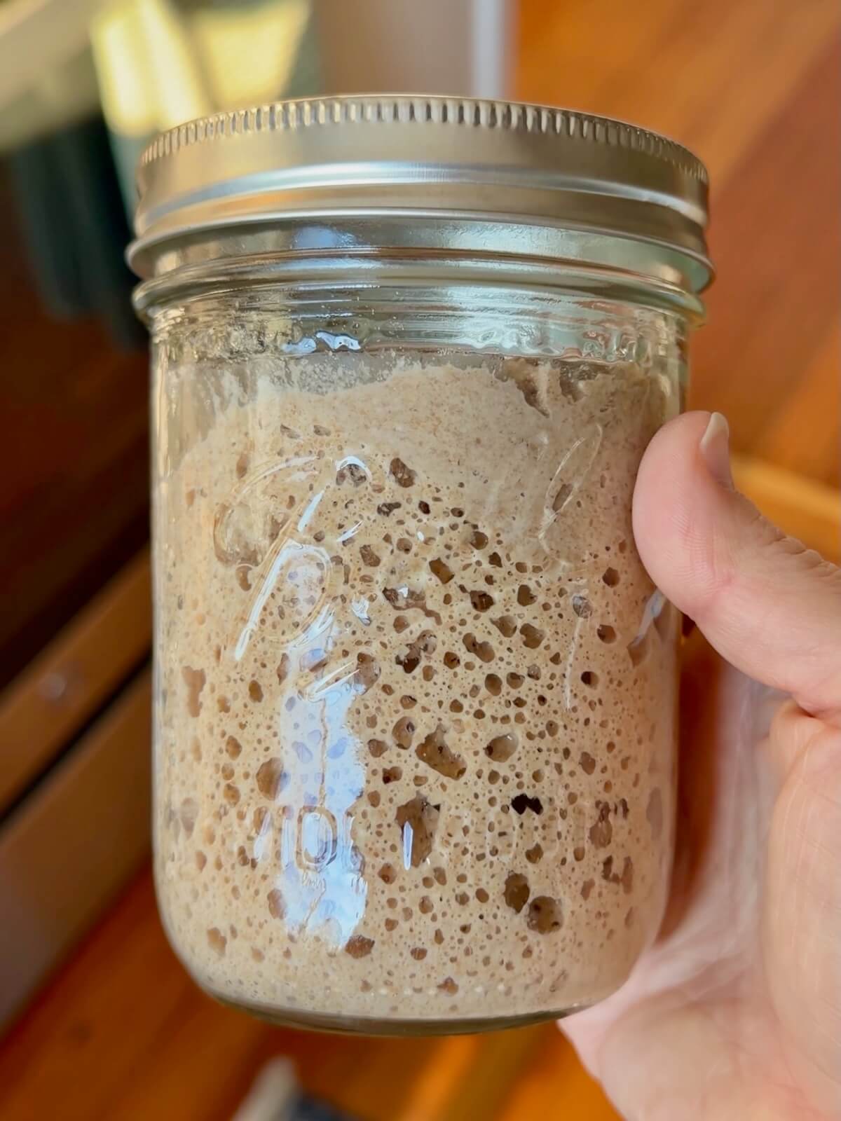 A very bubbly and active whole wheat sourdough starter in a glass mason jar.