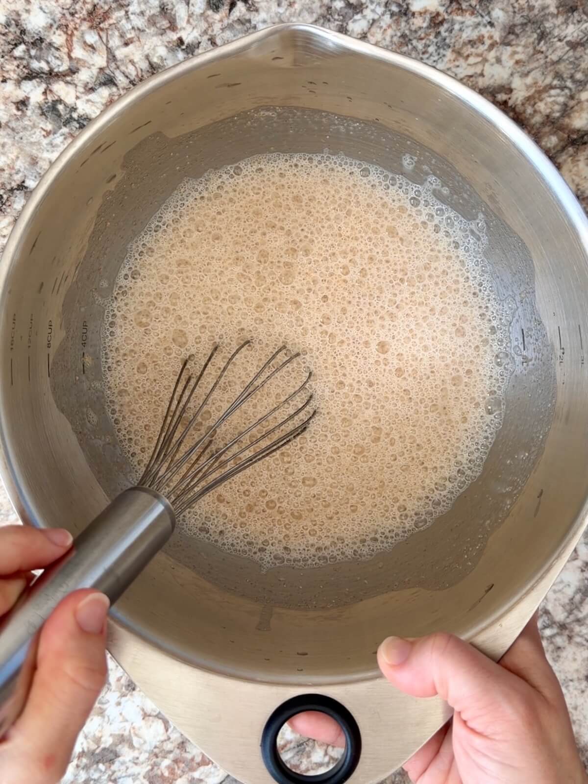Sourdough starter and water being whisked together in a stainless steel bowl.