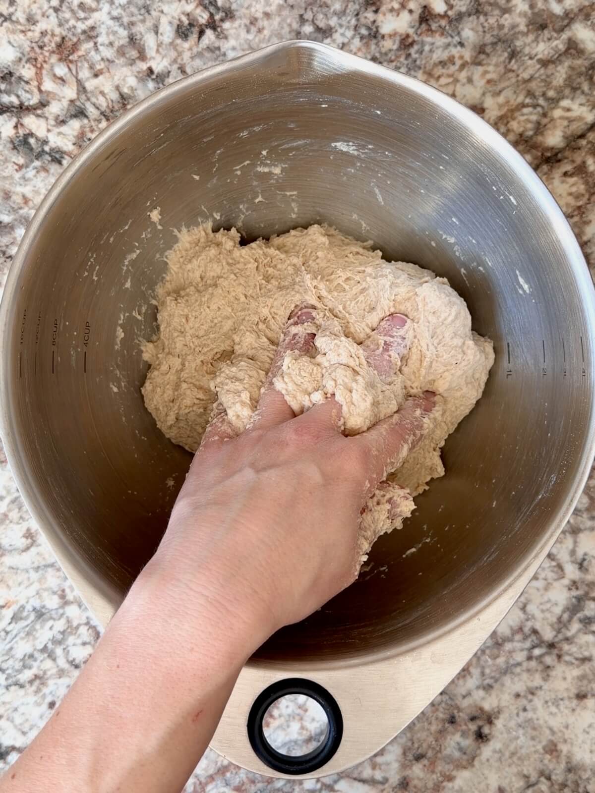 A hand mixing sourdough bread dough together in a stainless steel bowl.