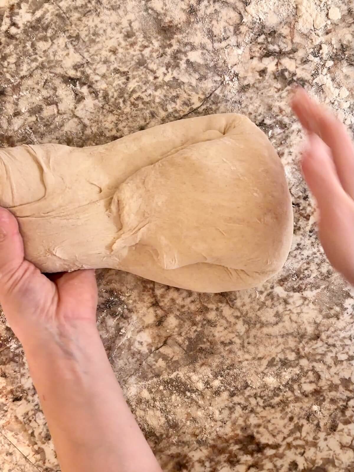 Two hands shaping sourdough bread dough into a ball on a floured counter.