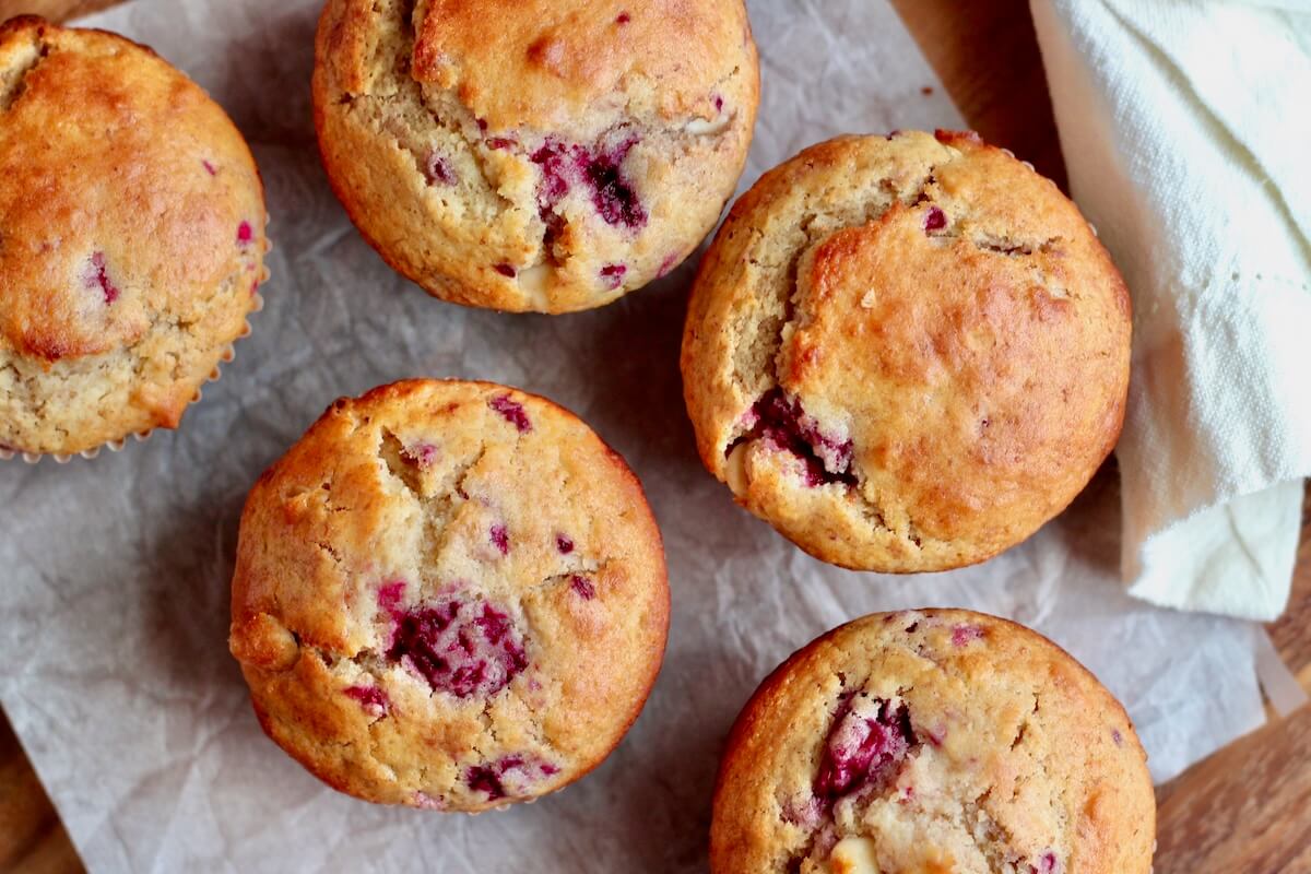 Five sourdough raspberry white chocolate muffins on a wrinkled piece of parchment paper.