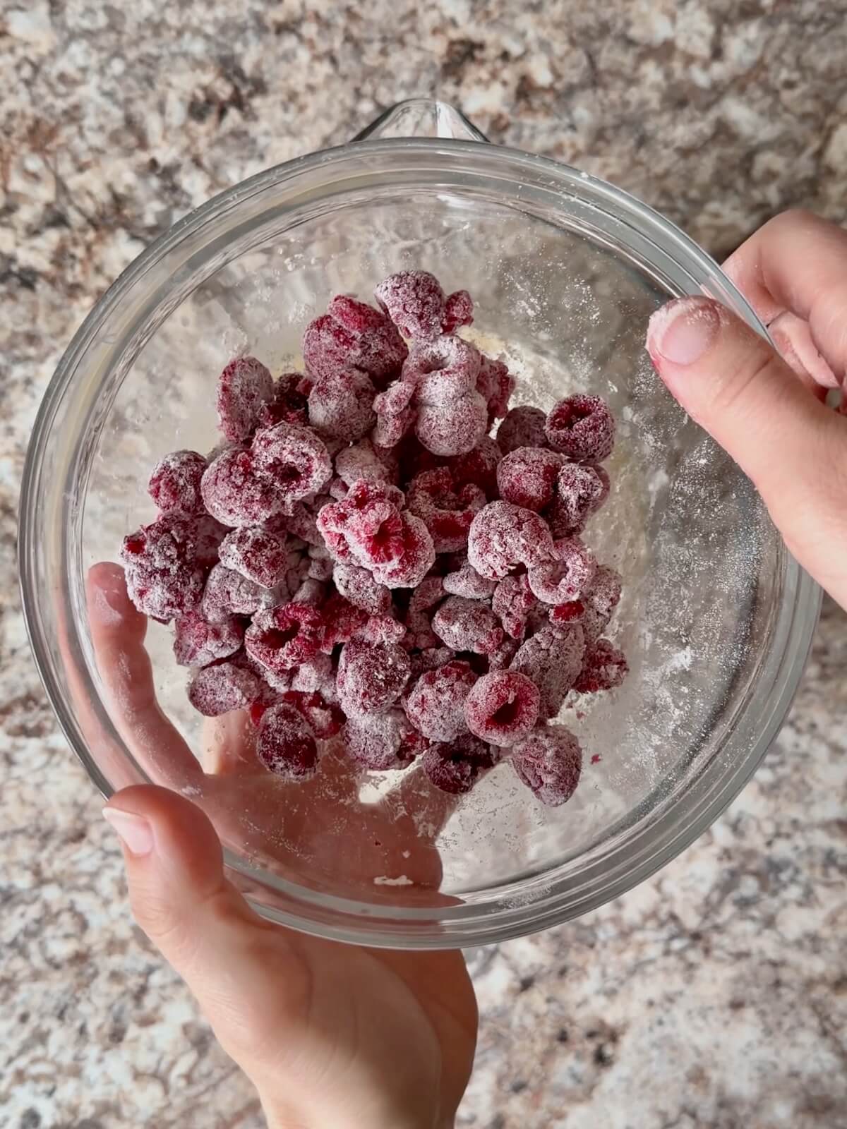 Frozen raspberries coated lightly in flour in a glass mixing bowl.