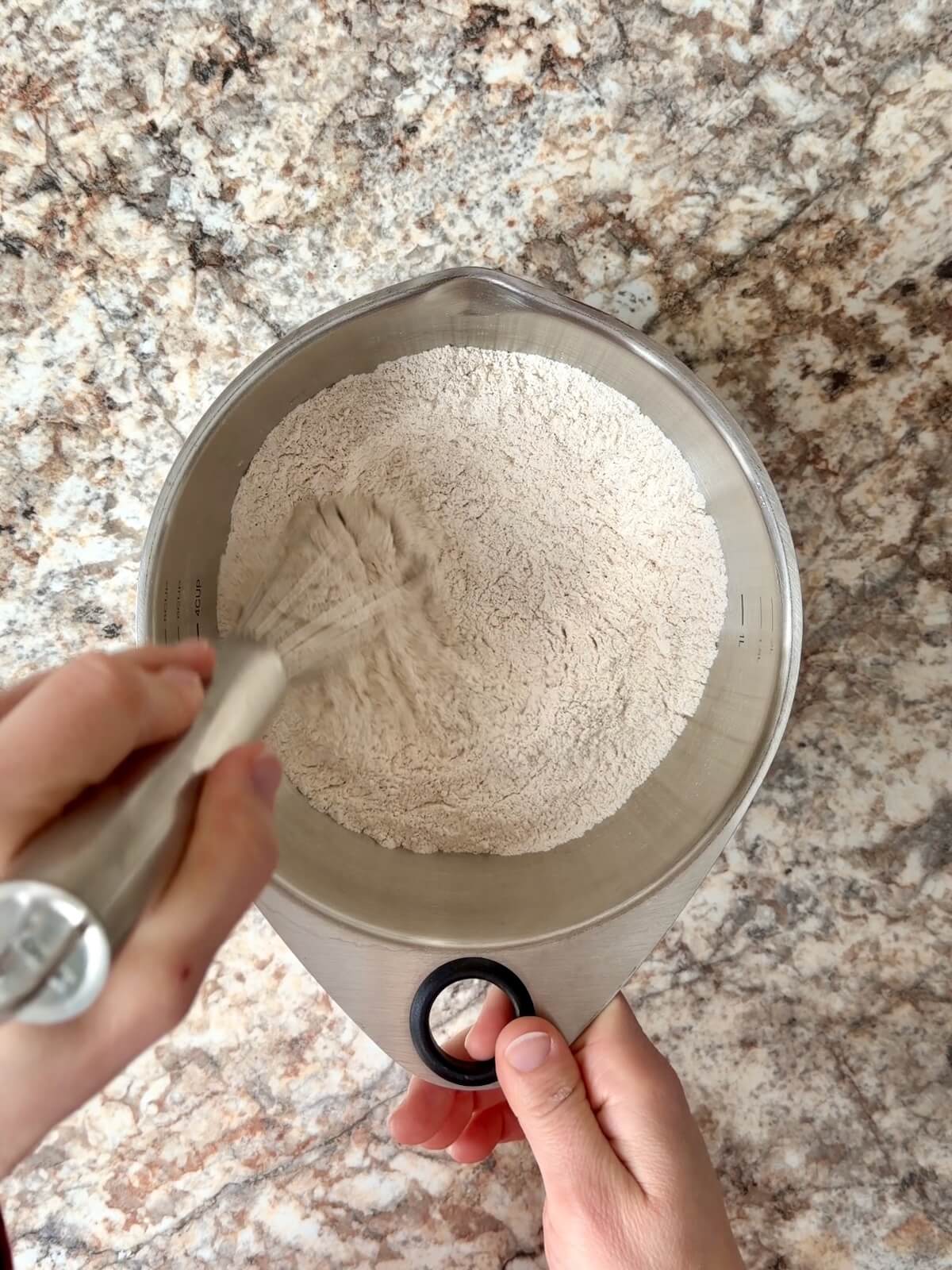 Flour and other dry ingredients being whisked together in a bowl.