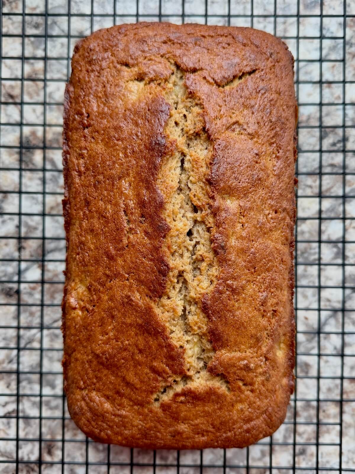 A baked loaf of sourdough discard banana bread on a wire cooling rack.