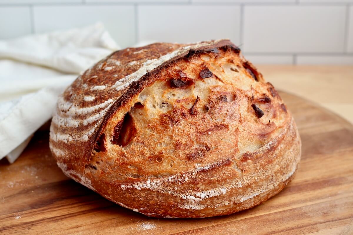 A whole loaf of freeze-dried strawberry sourdough bread on a wooden cutting board.