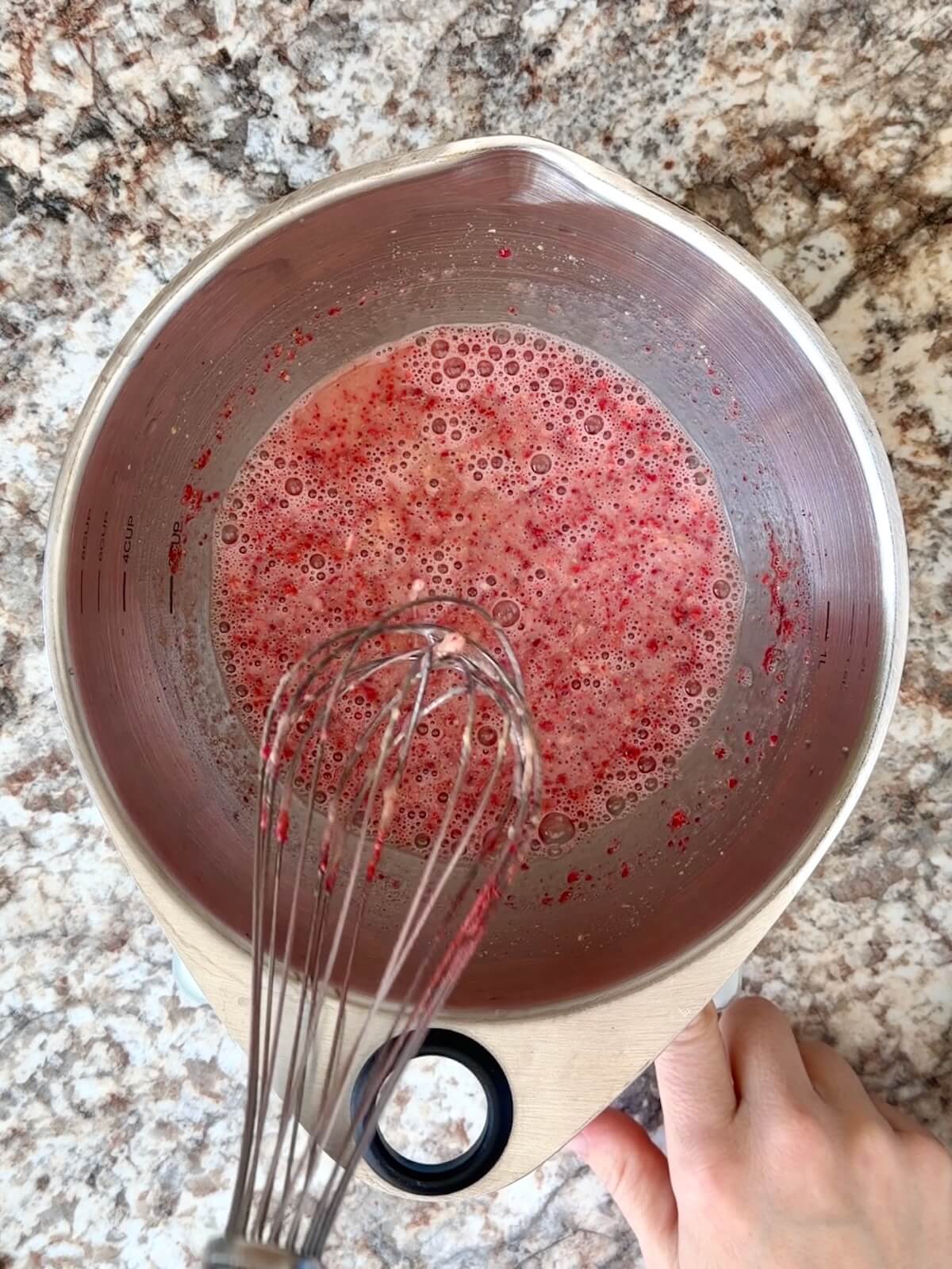 Crushed freeze-dried strawberries whisked together with active sourdough starter and water in a stainless steel bowl.