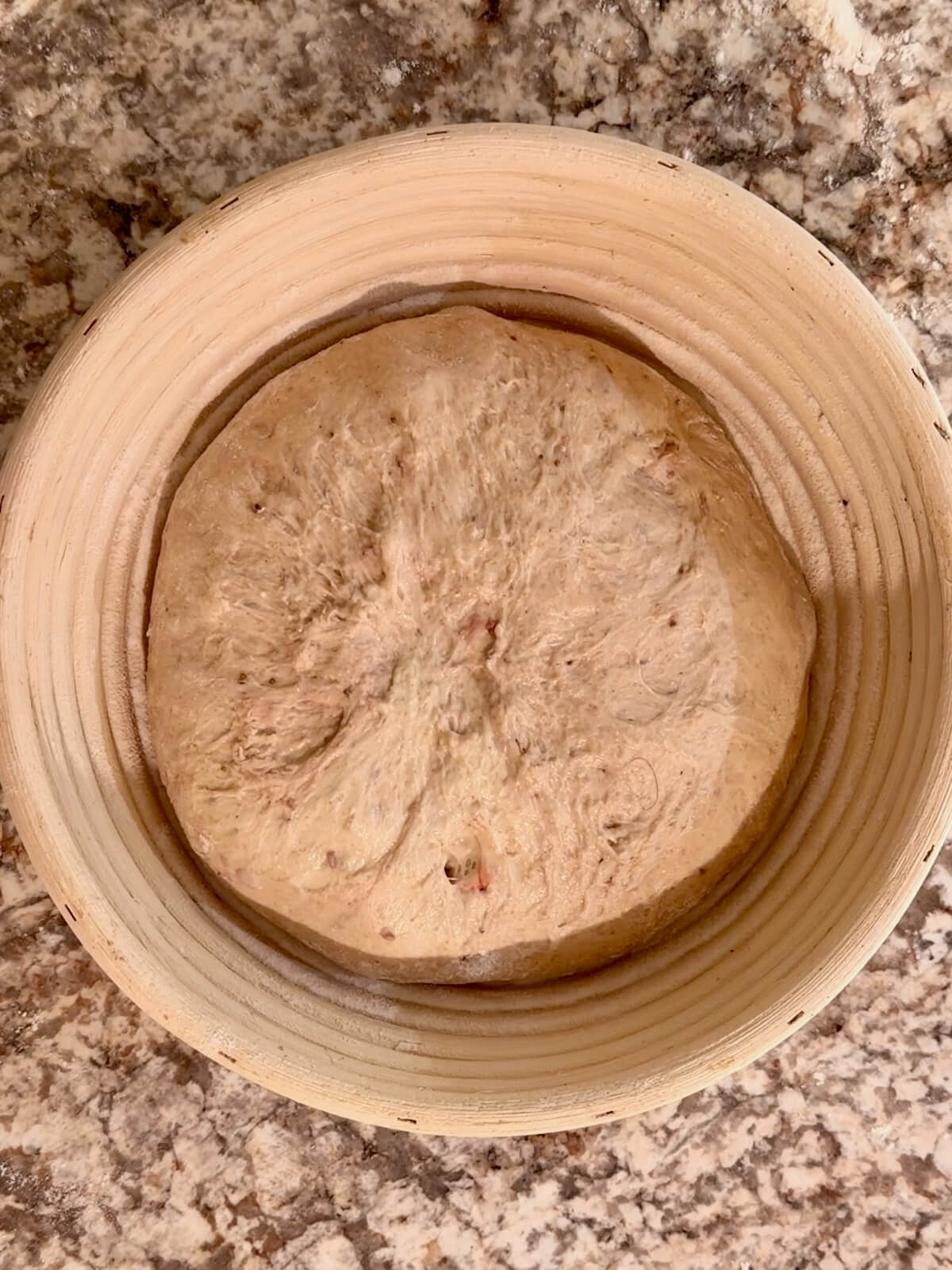 Strawberry sourdough bread dough in a round proofing basket.