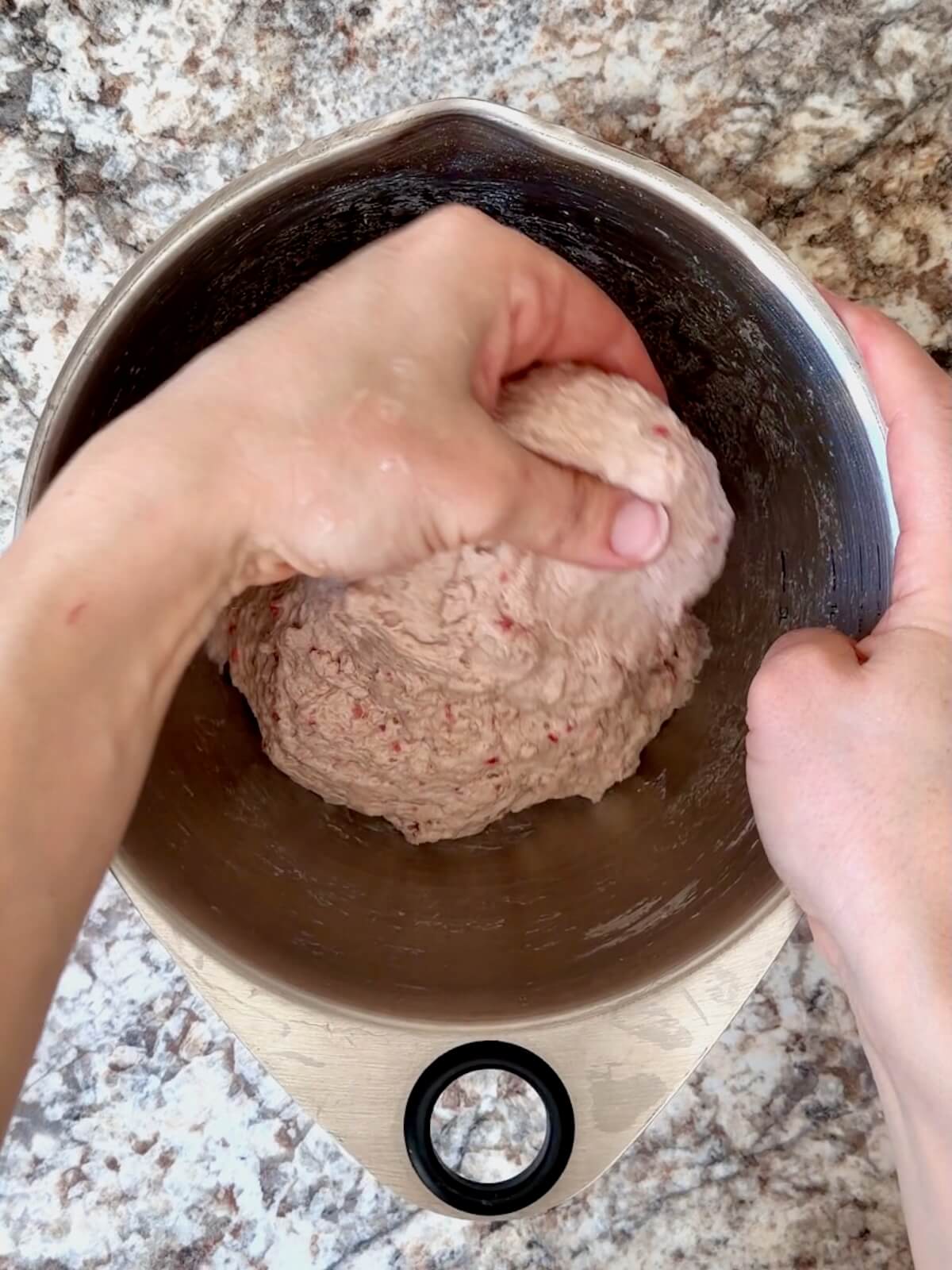 Strawberry sourdough bread dough being stretched and folded in a stainless steel bowl.