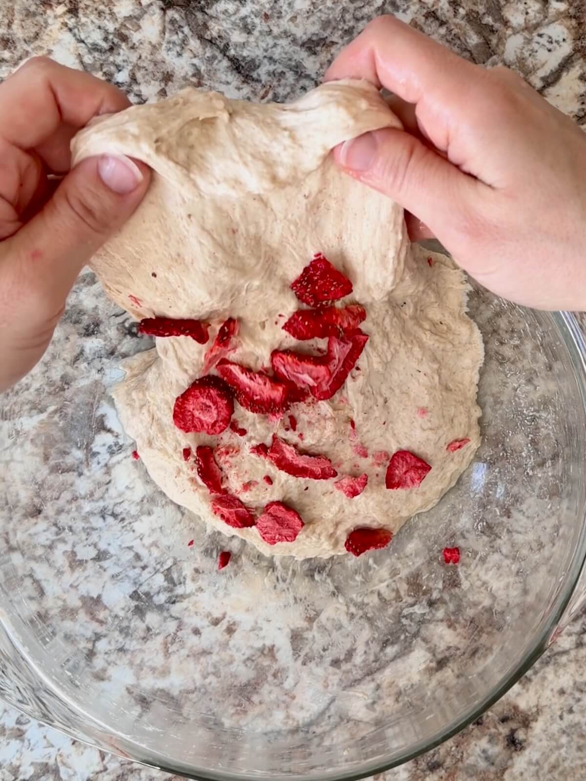 Sourdough bread dough with pieces of freeze-dried strawberries being stretched and folded into the dough.