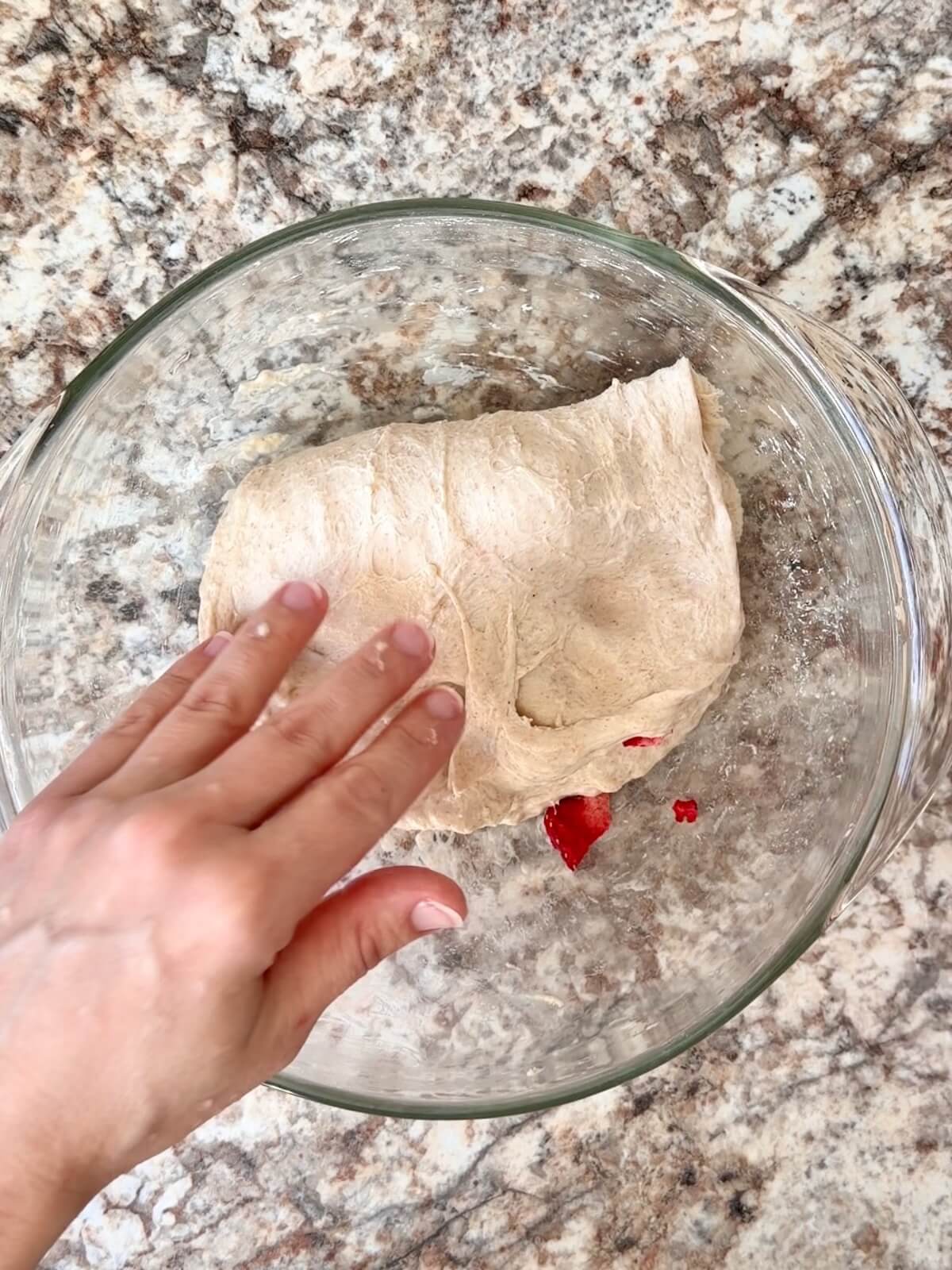 Sourdough bread dough with pieces of freeze-dried strawberries being stretched and folded into the dough.