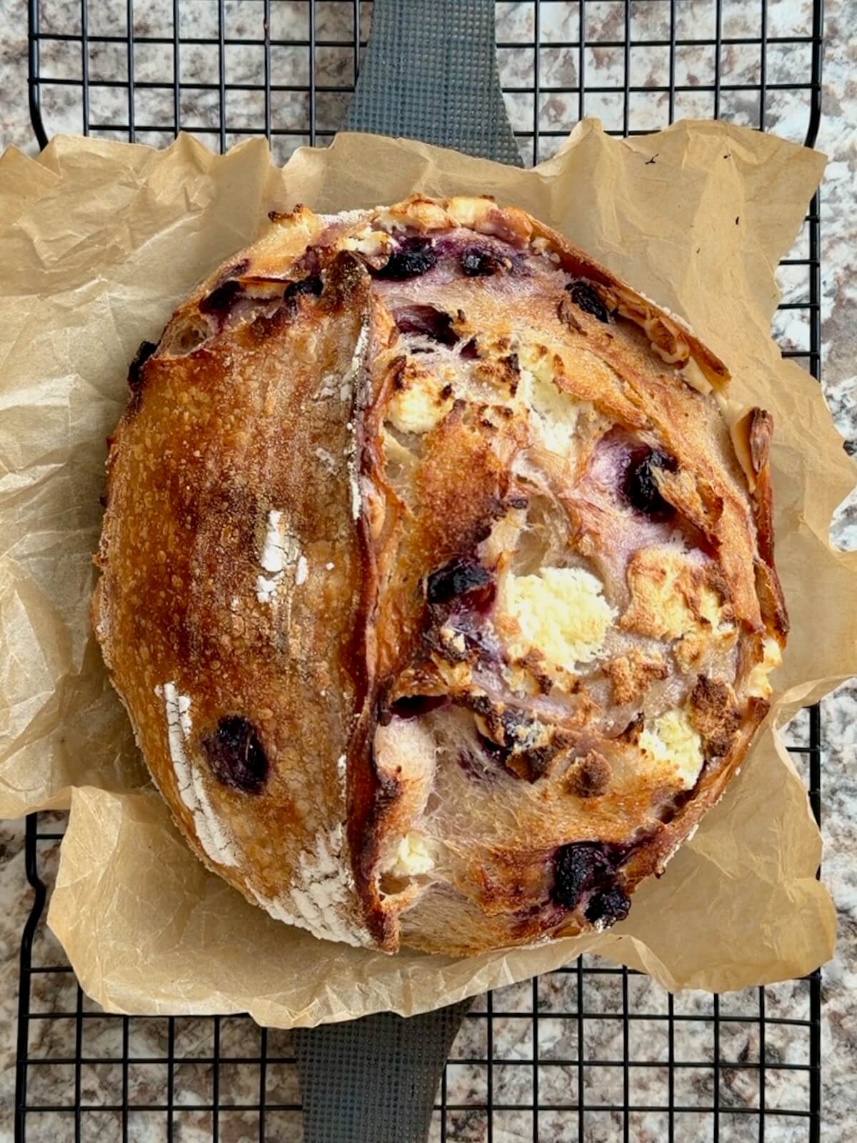 A baked loaf of blueberry cream cheese sourdough bread on a wire cooling rack.