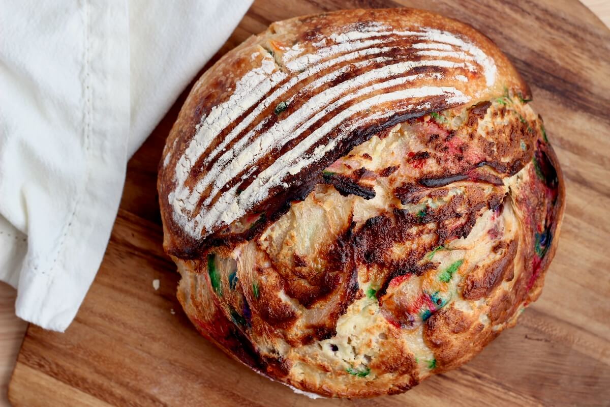 A whole loaf of funfetti sourdough bread with cream cheese frosting on a wooden cutting board.