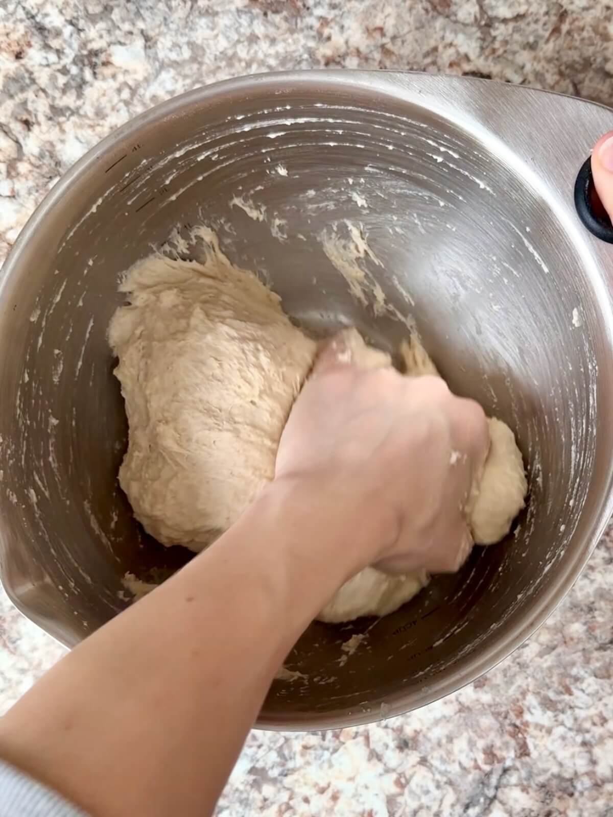 Sourdough bread dough being mixed by hand in a stainless steel bowl.