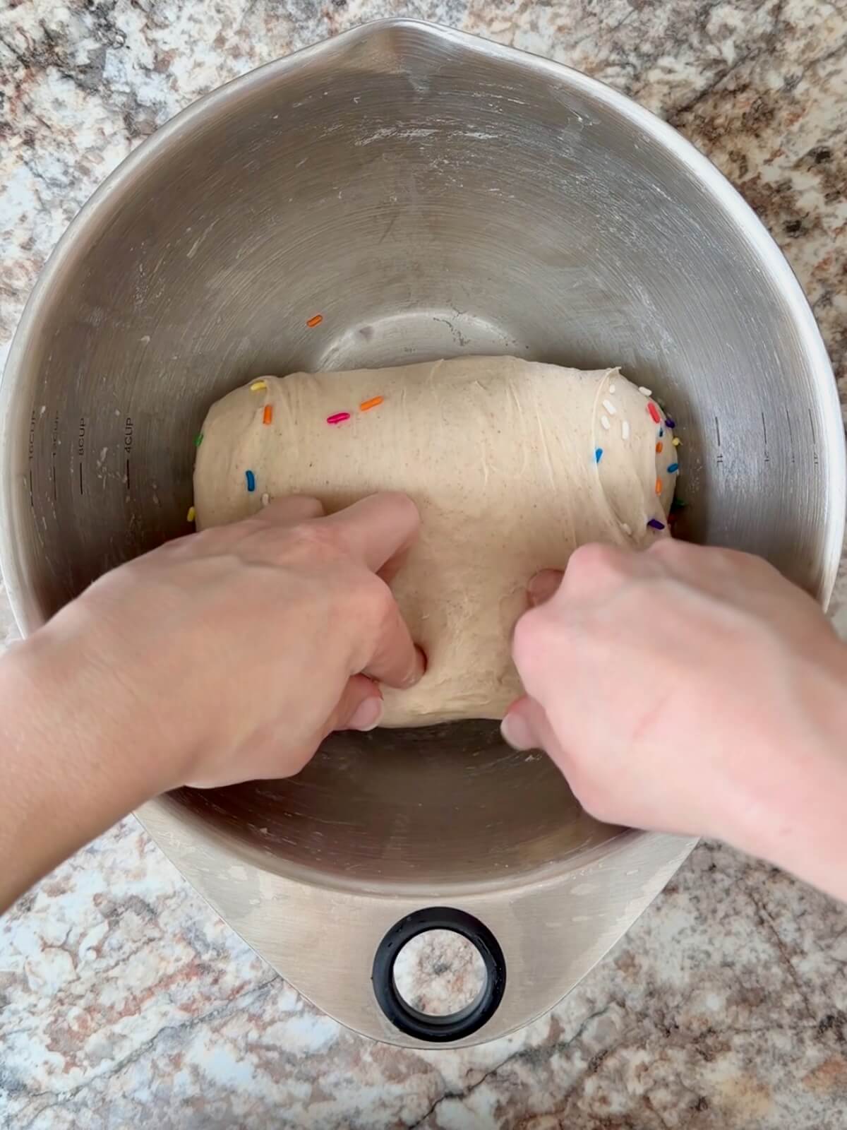 Funfetti sourdough bread dough being stretched and folded in a bowl.