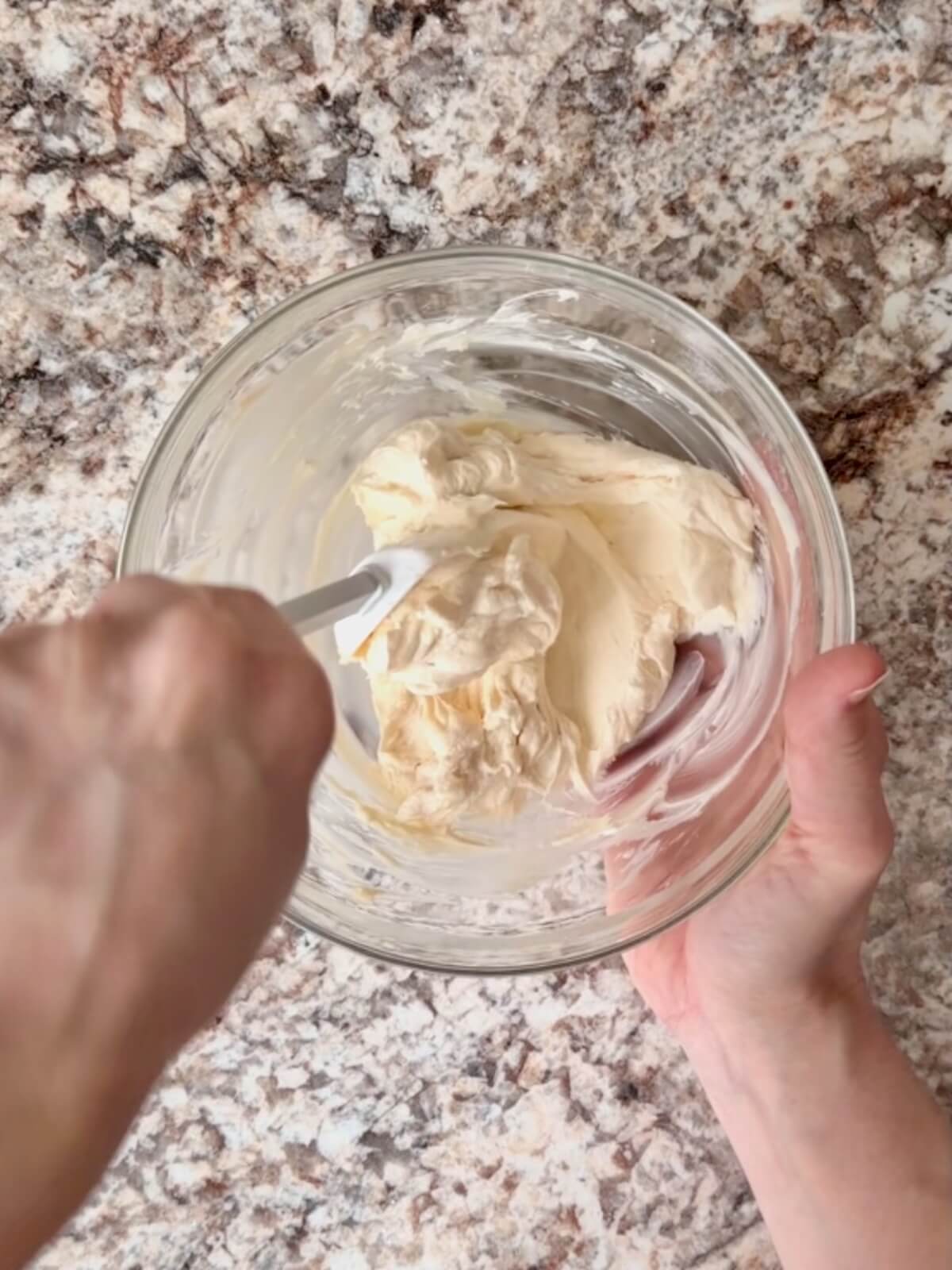 Softened cream cheese and powdered sugar being mixed together in a small glass bowl.
