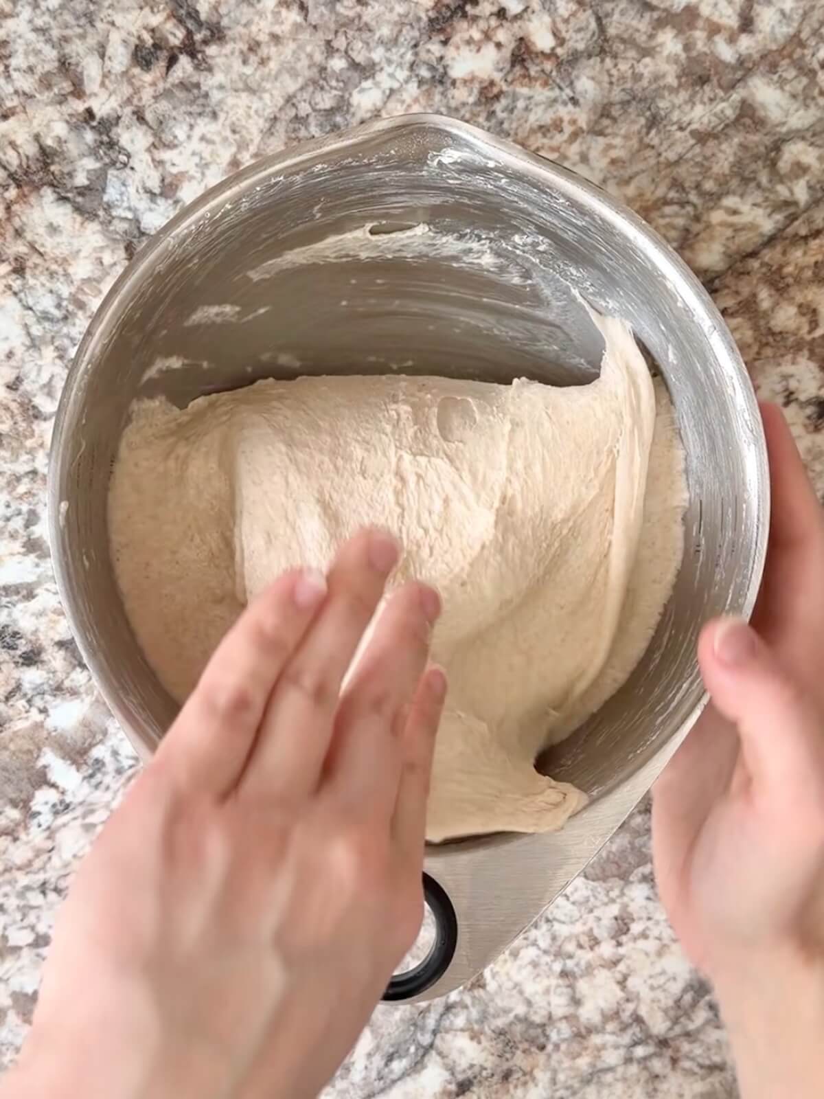 Sourdough focaccia dough being stretched and folded in a stainless steel bowl.