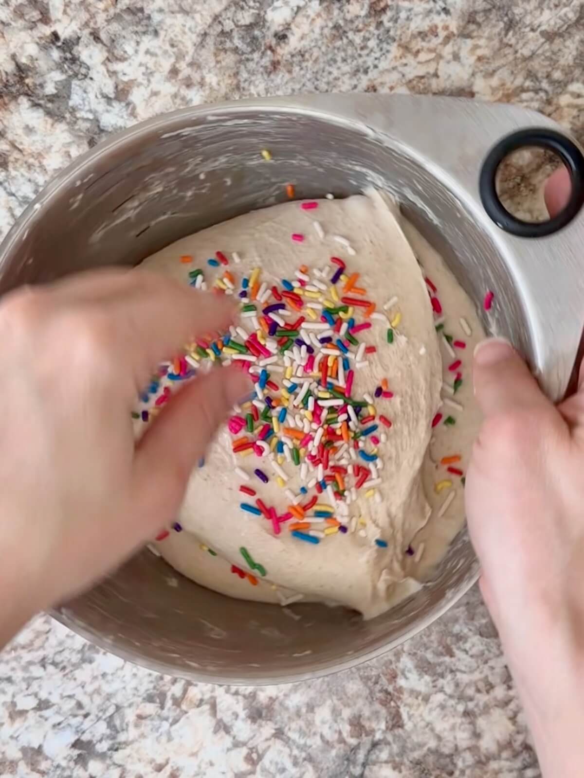 Sprinkles being added to the sourdough focaccia dough in a stainless steel bowl.
