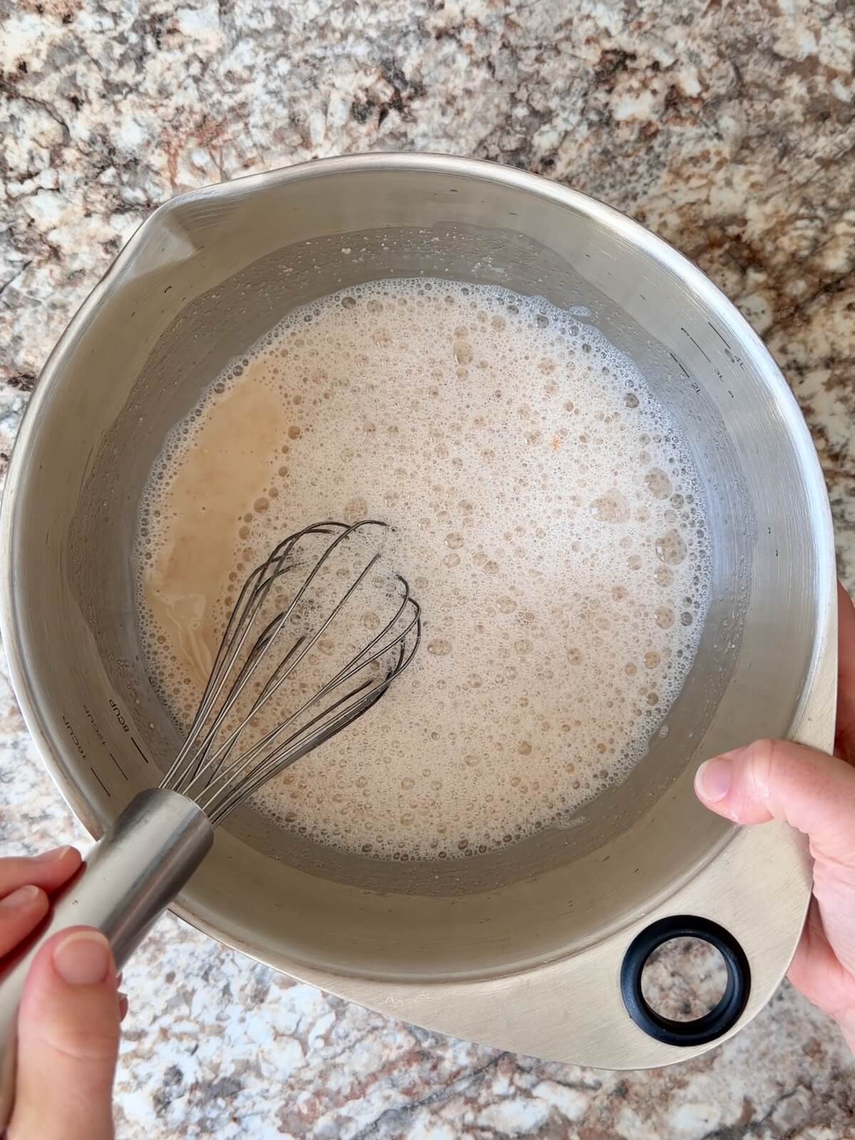 Active sourdough starter and water whisked together in a stainless steel bowl.