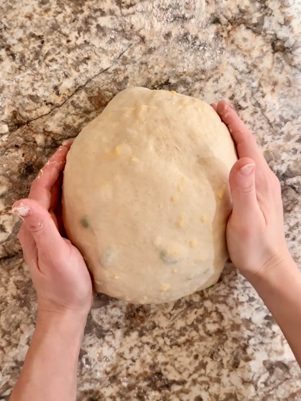 JalapeƱo cheddar sourdough bread dough being shaped into a round boule on a floured counter.