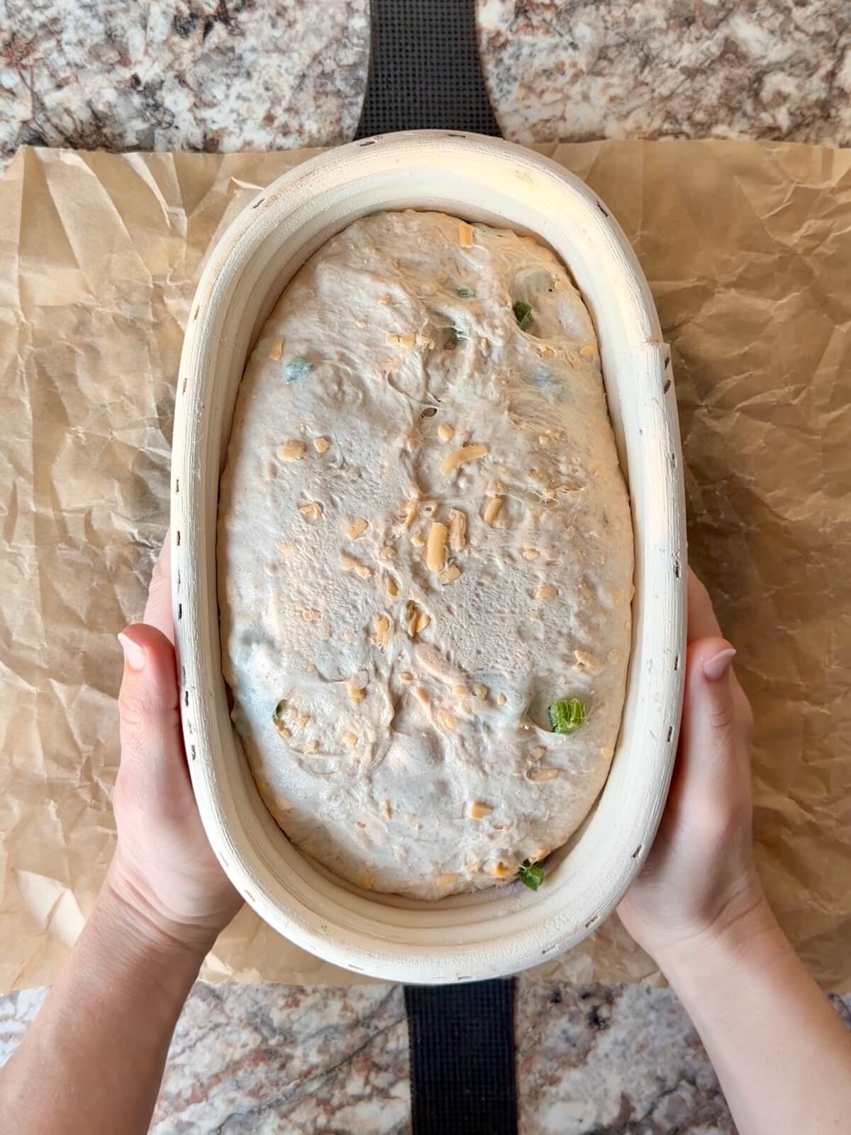 JalapeƱo cheddar sourdough bread dough in an oval proofing basket after cold proofing overnight.