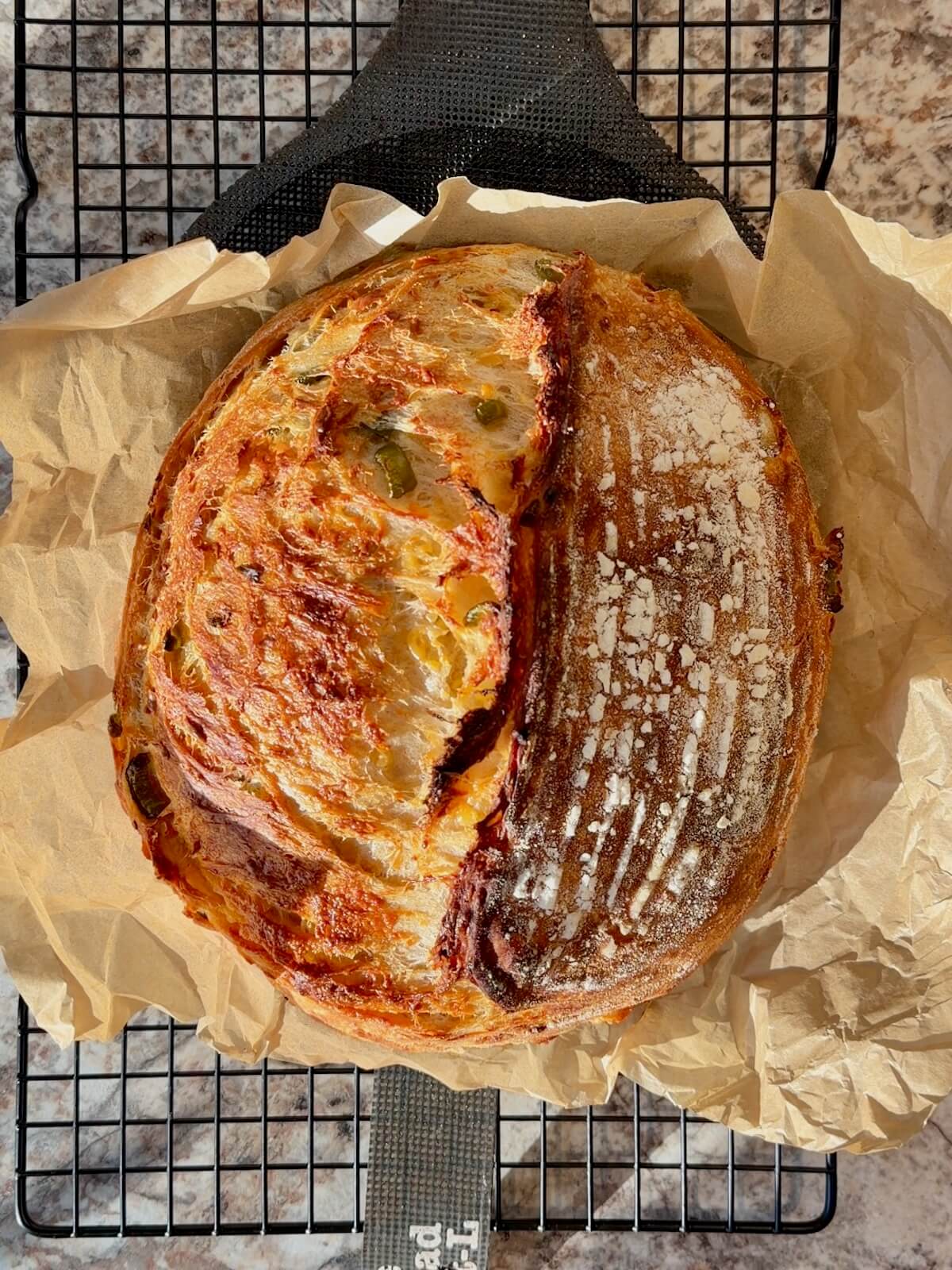 A baked loaf of jalapeƱo cheddar sourdough bread on a wire cooling rack.