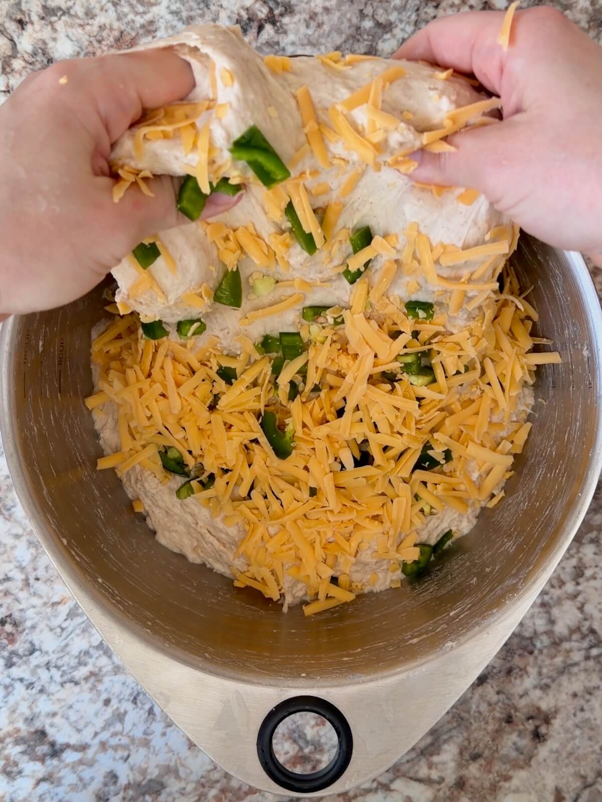 Fresh jalapeƱos and shredded cheddar cheese being folded into sourdough bread dough.