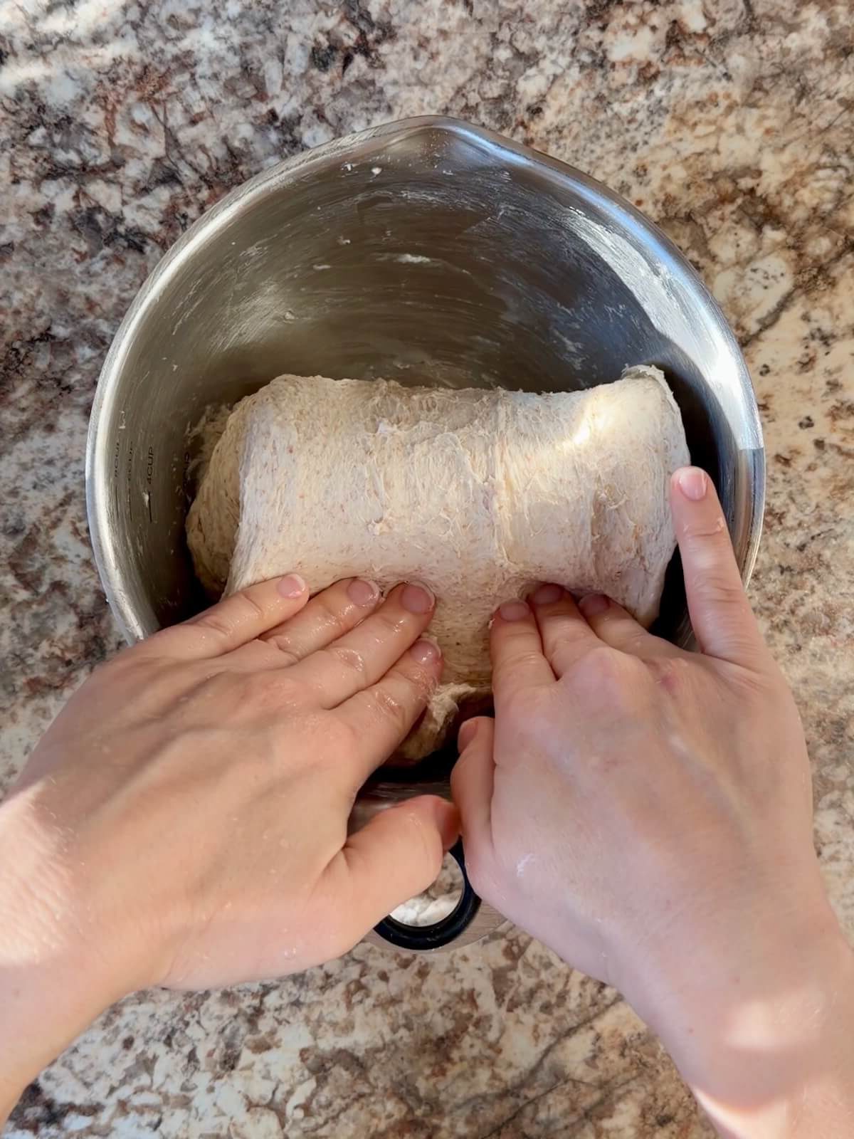Two hands folding one edge of the dough over itself in a bowl.