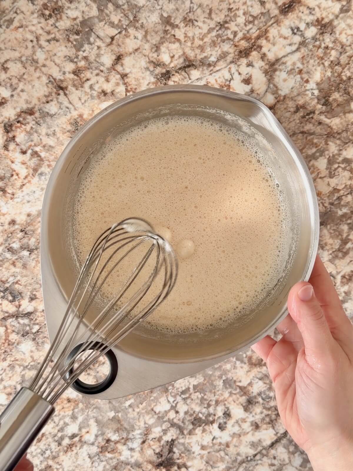 Beer and active sourdough starter whisked together in a stainless steel bowl.