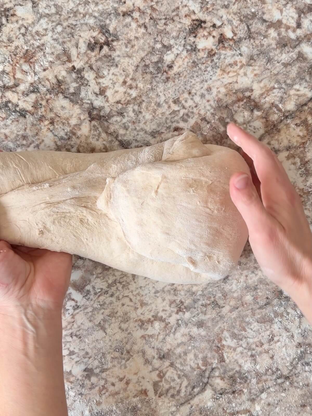 Beer sourdough bread dough being shaped on a floured counter.