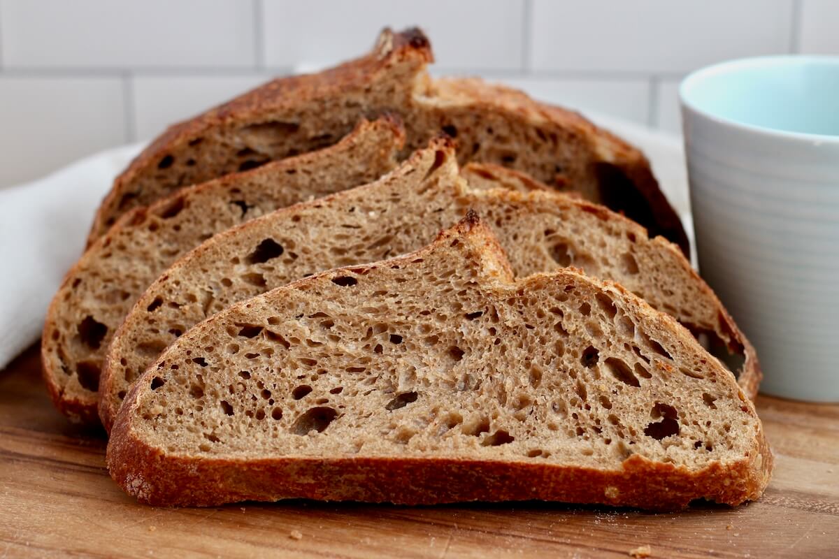 A sliced loaf of coffee sourdough bread on a cutting board next to a blue ceramic mug.