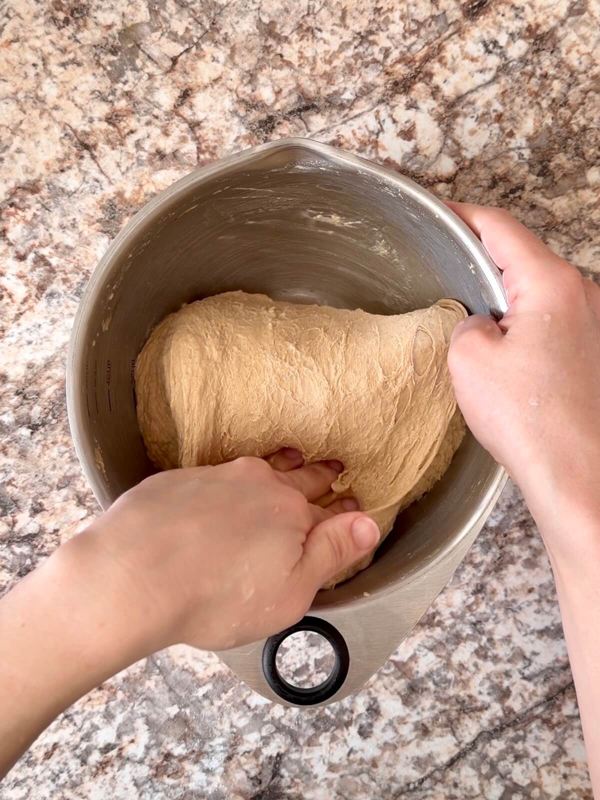 Two hands folding the dough over on top of itself in a mixing bowl.