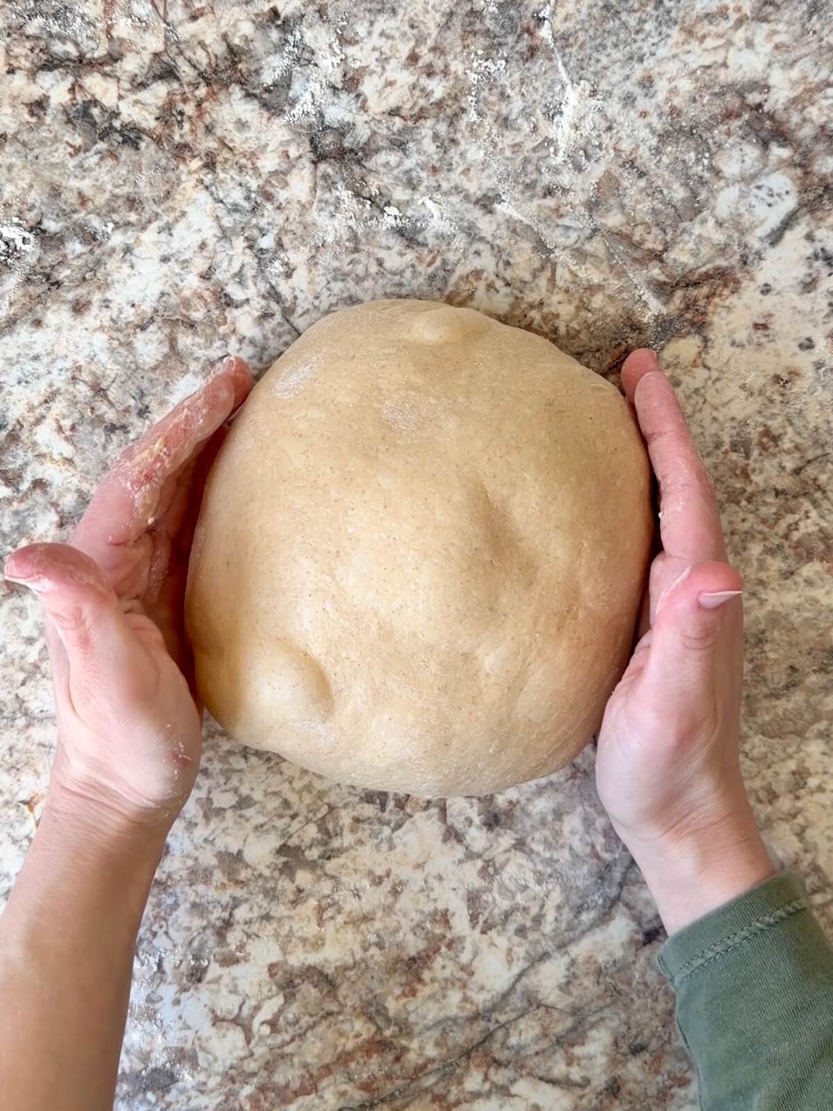 Two hands rounding the coffee sourdough bread dough into a ball on a floured counter.