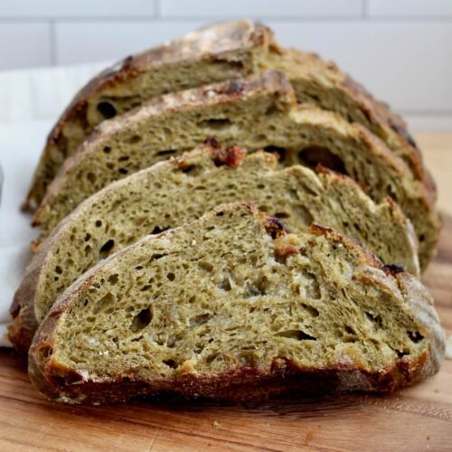 Slices of white chocolate matcha sourdough bread on a wooden cutting board.