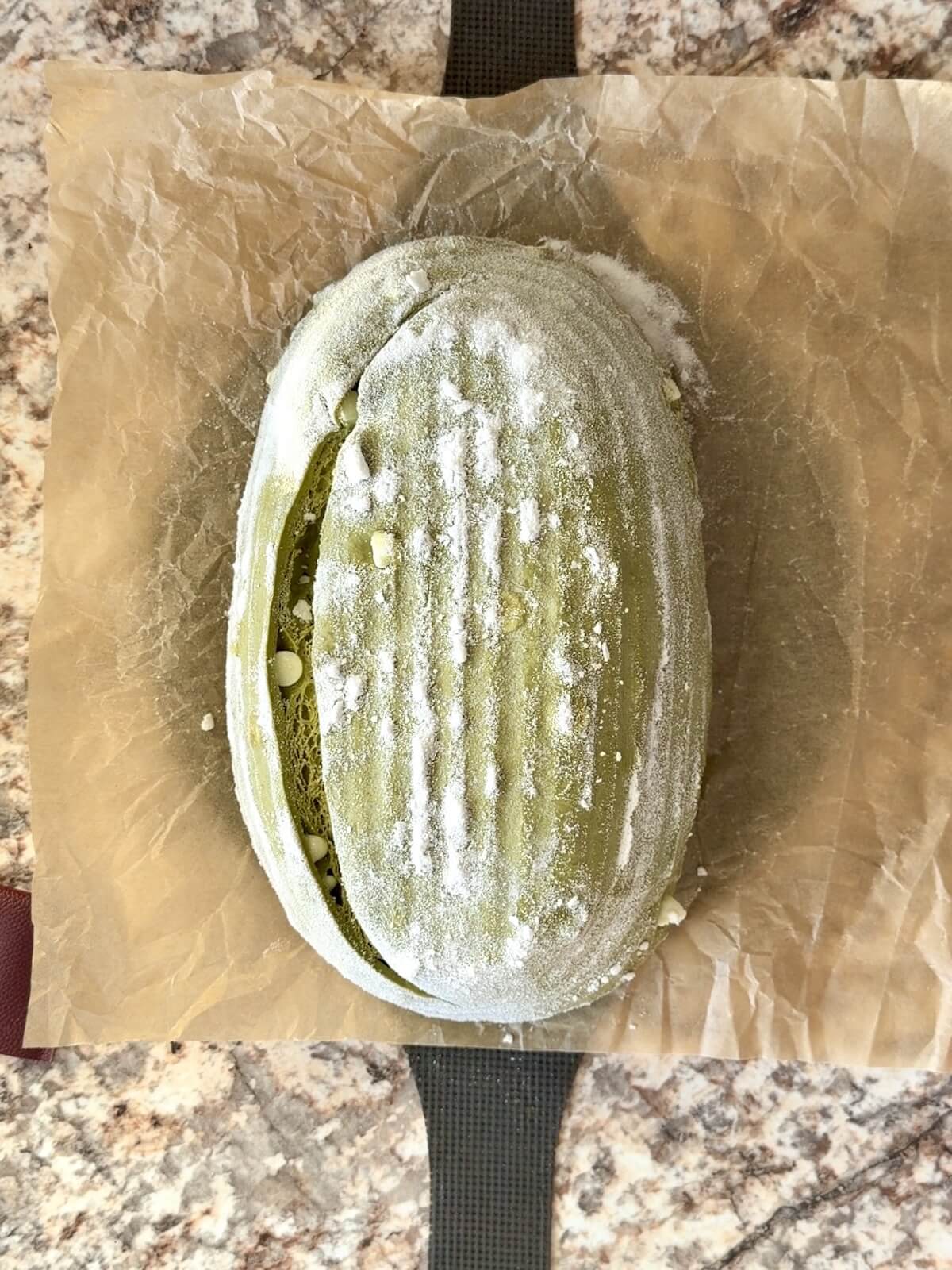 A scored matcha sourdough bread dough on a piece of parchment paper.