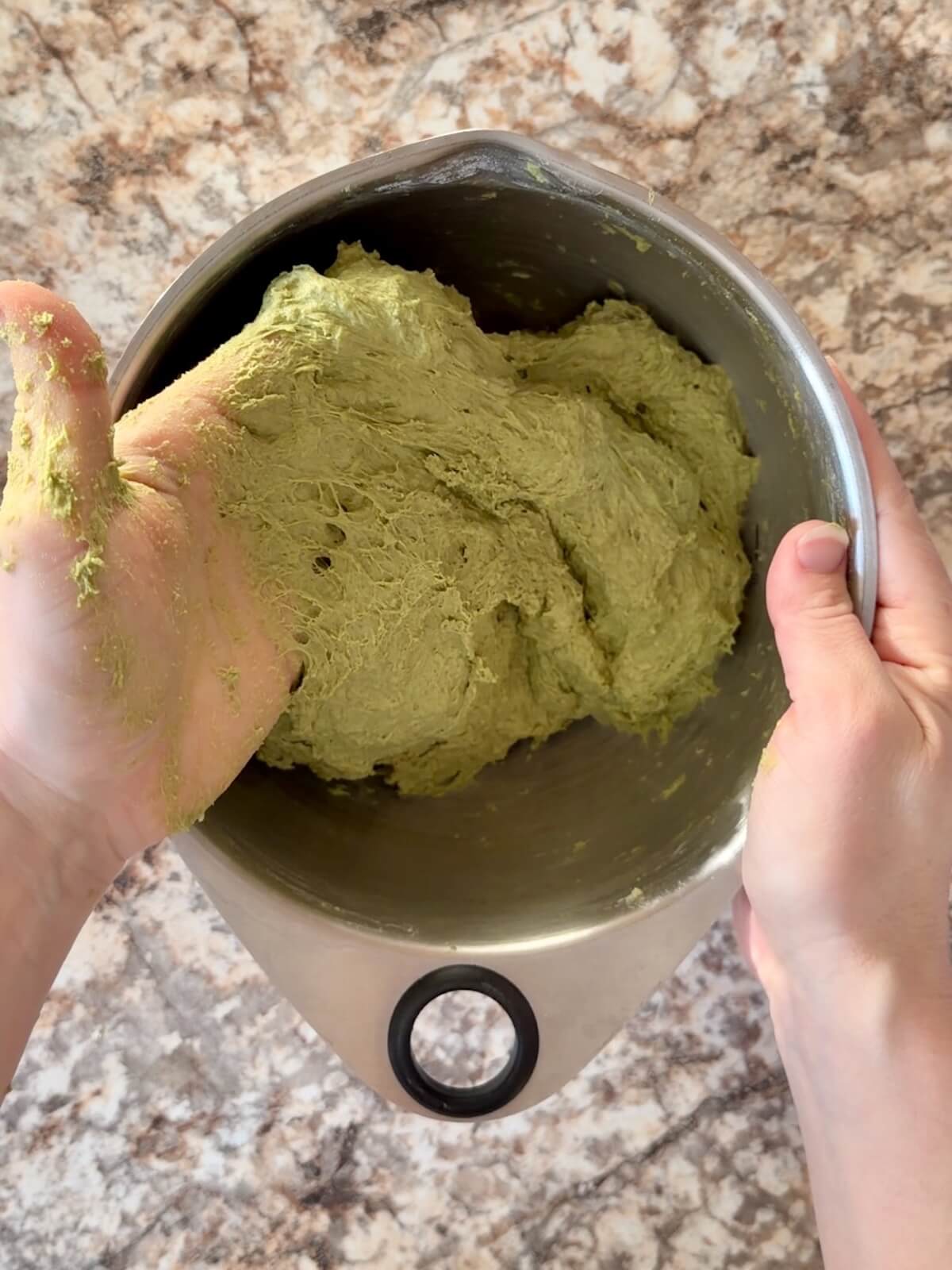Matcha sourdough bread dough being mixed by hand in a bowl.