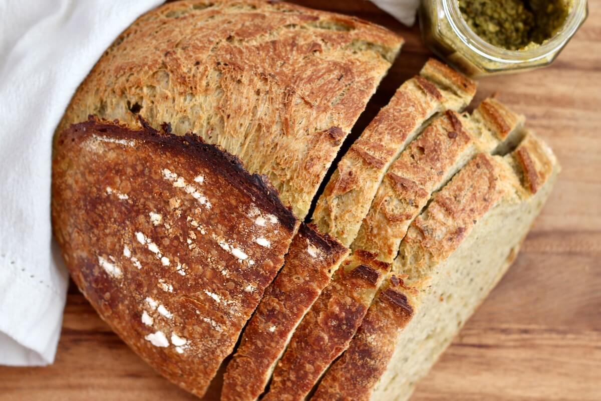 A loaf of pesto sourdough bread with three slices cut from it.