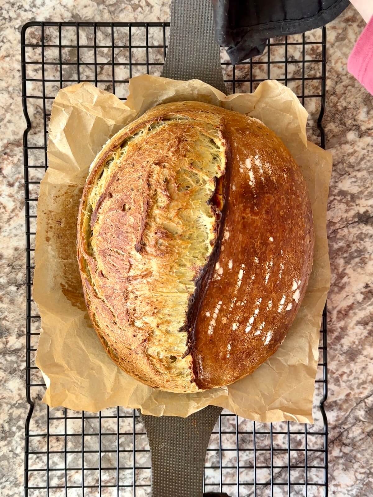 A baked loaf of pesto sourdough bread on a wire cooling rack.