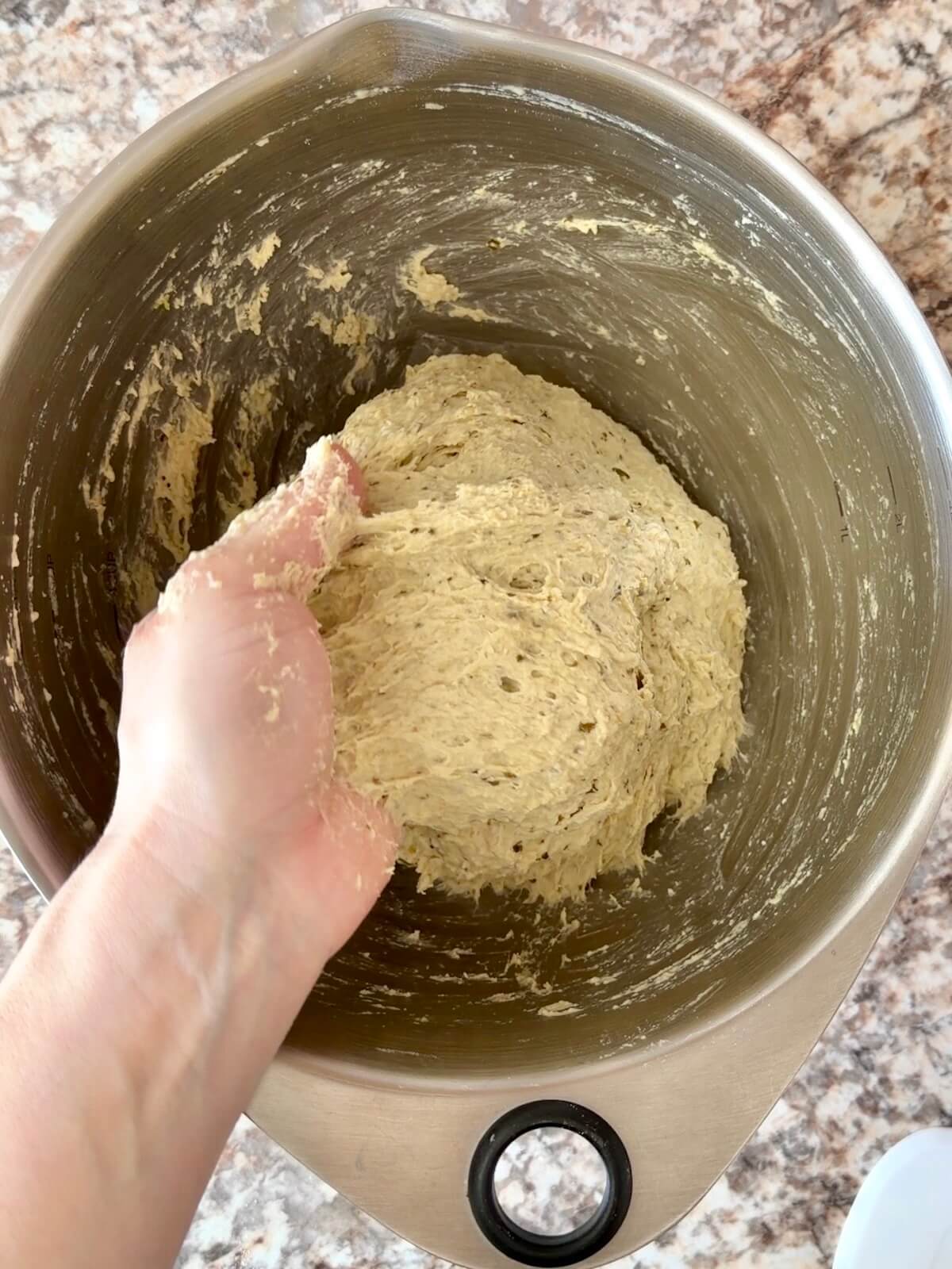Pesto sourdough bread dough being mixed by hand in a bowl.