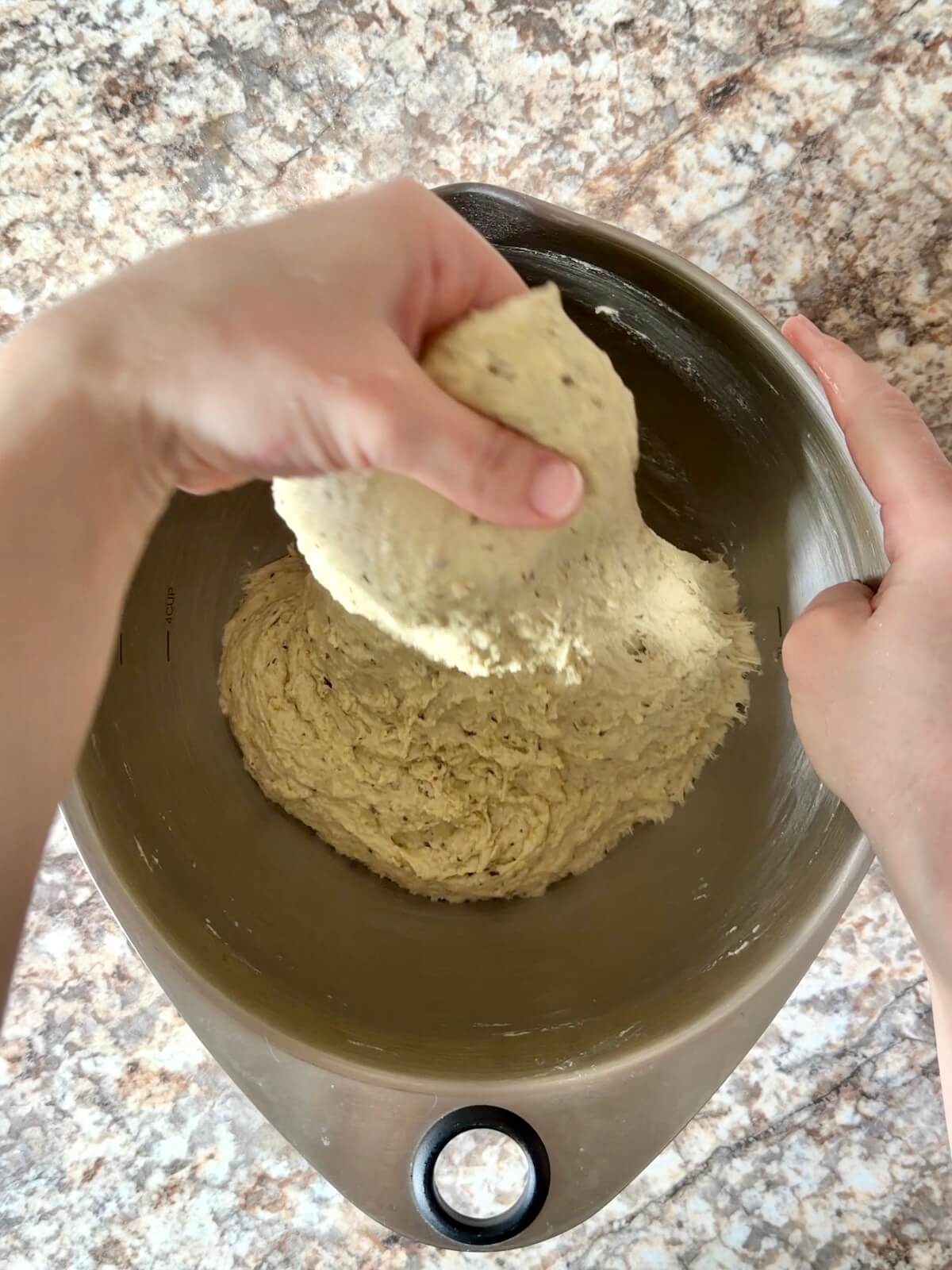 Pesto sourdough bread dough being stretched up out of the mixing bowl.