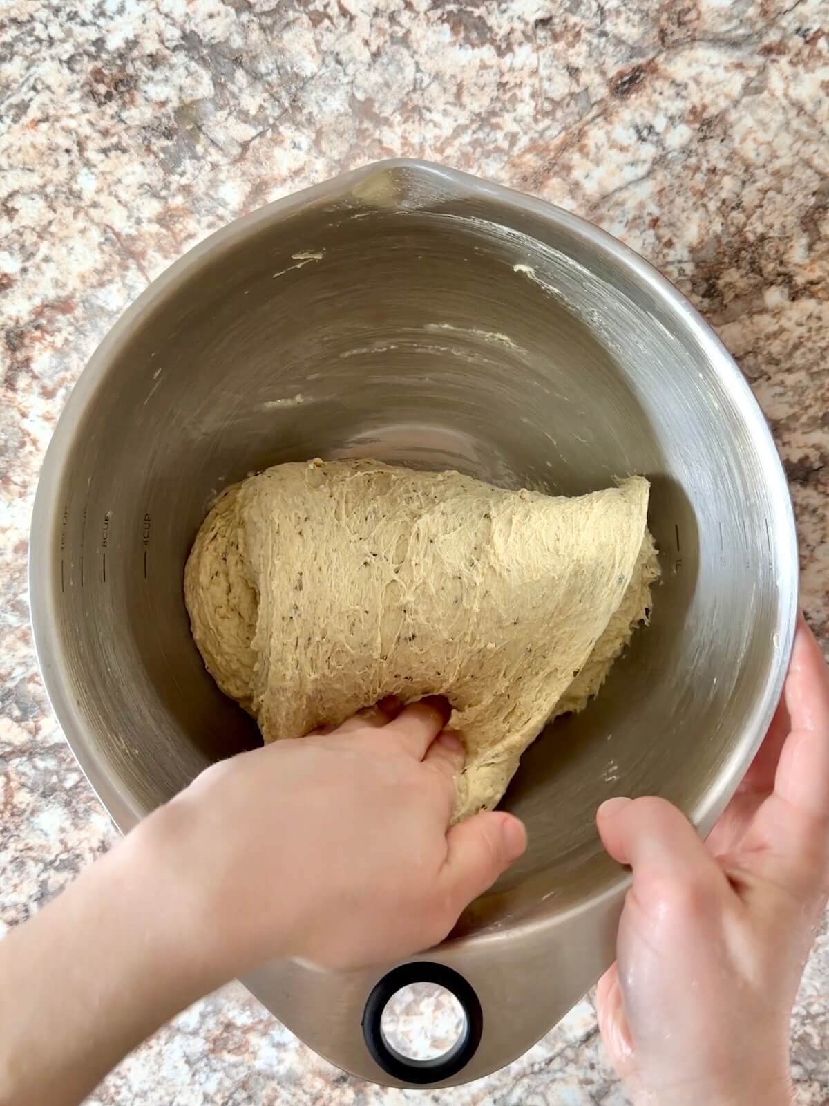 Pesto sourdough bread dough being folded over itself in a mixing bowl.