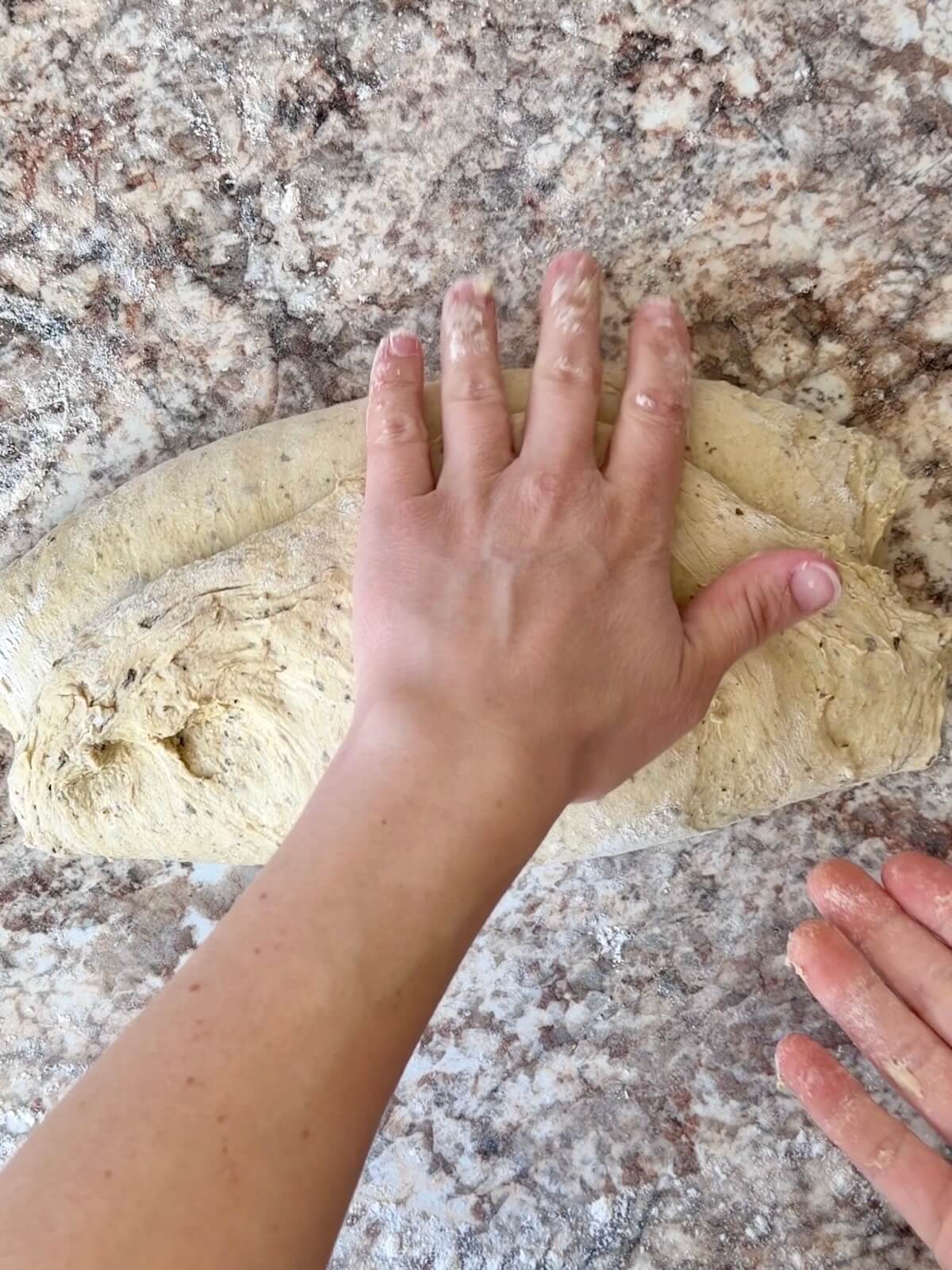 Two hands shaping pesto sourdough bread dough by folding it into thirds.