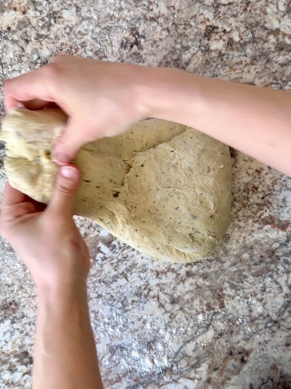 Two hands shaping sourdough bread dough by folding all four edges towards the center.