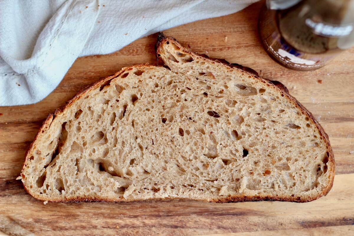 A single slice of root beer sourdough bread on a wooden cutting board.