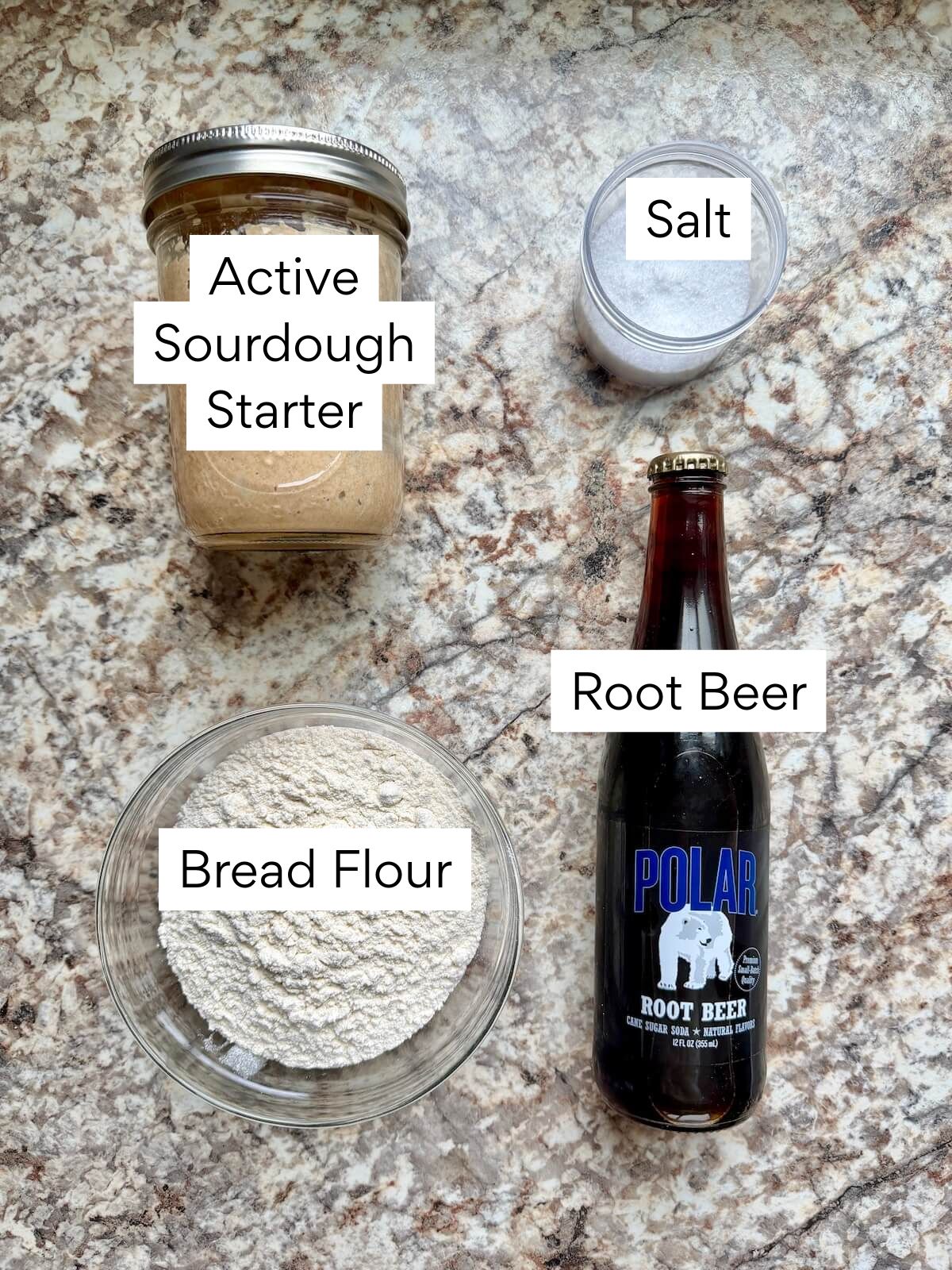 The ingredients to make root beer sourdough bread. Each ingredient is labeled with text. They include active sourdough starter, bread flour, salt, and root beer.