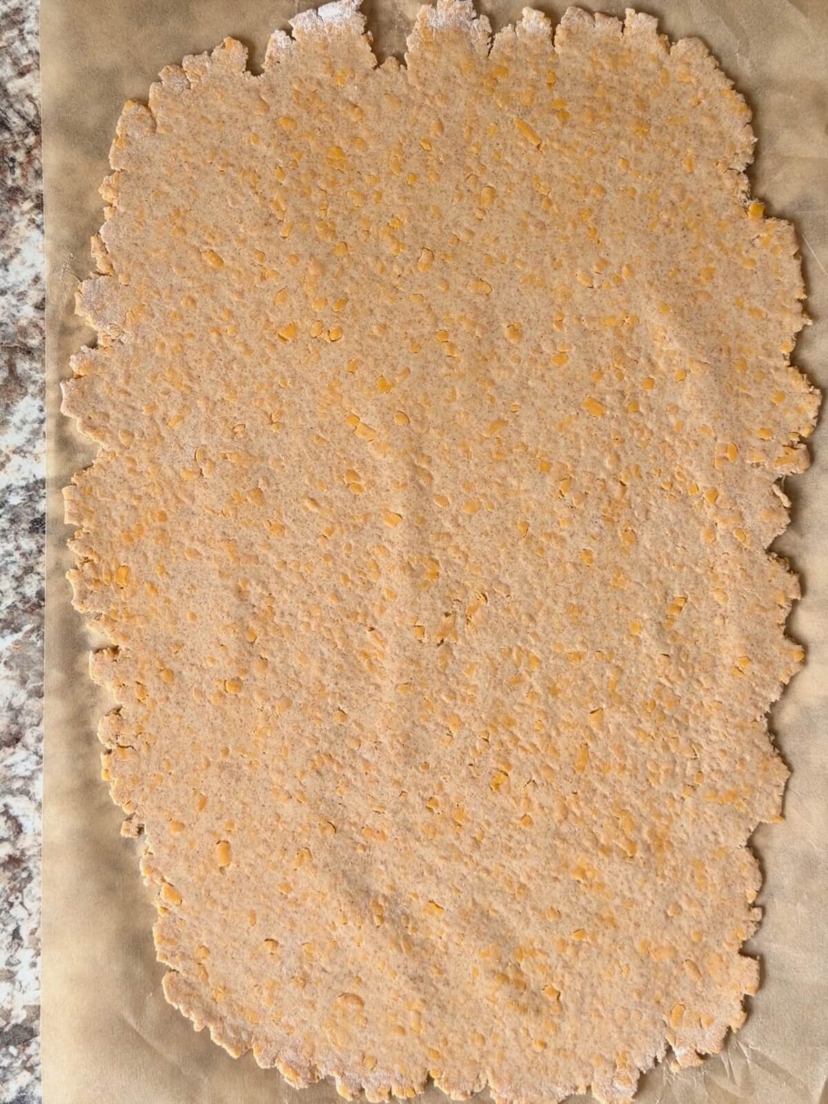 Sourdough cheese cracker dough rolled out onto a sheet of parchment paper.